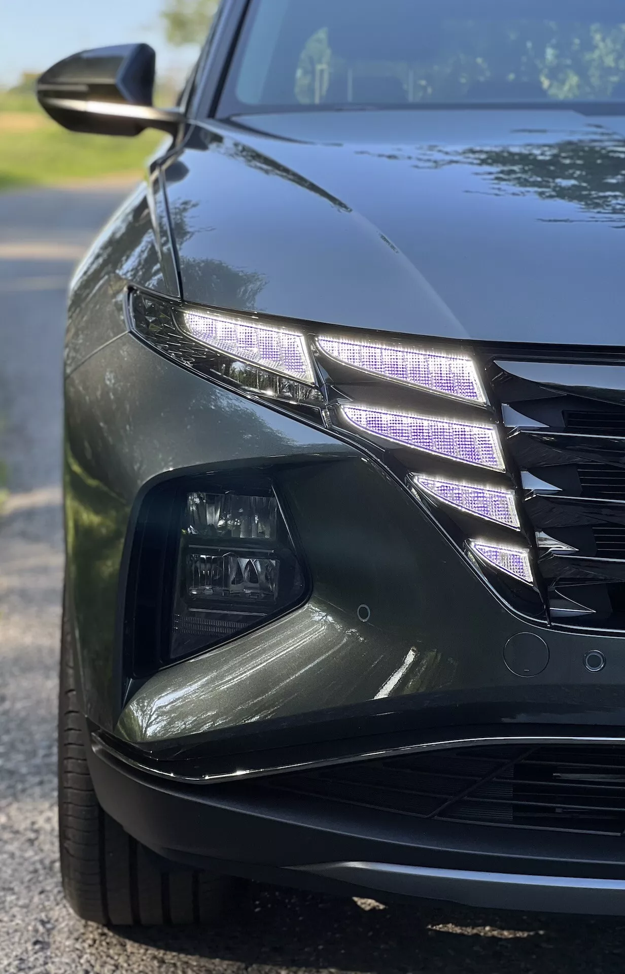 Vue rapprochée et angulaire d'une Hyundai Tucson 2020 montrant un design complexe des phares LED et une partie de la grille avec une finition brillante dans des conditions de faible luminosité, illustrant les caractéristiques des voitures de luxe et la technologie moderne de l'éclairage automobile.