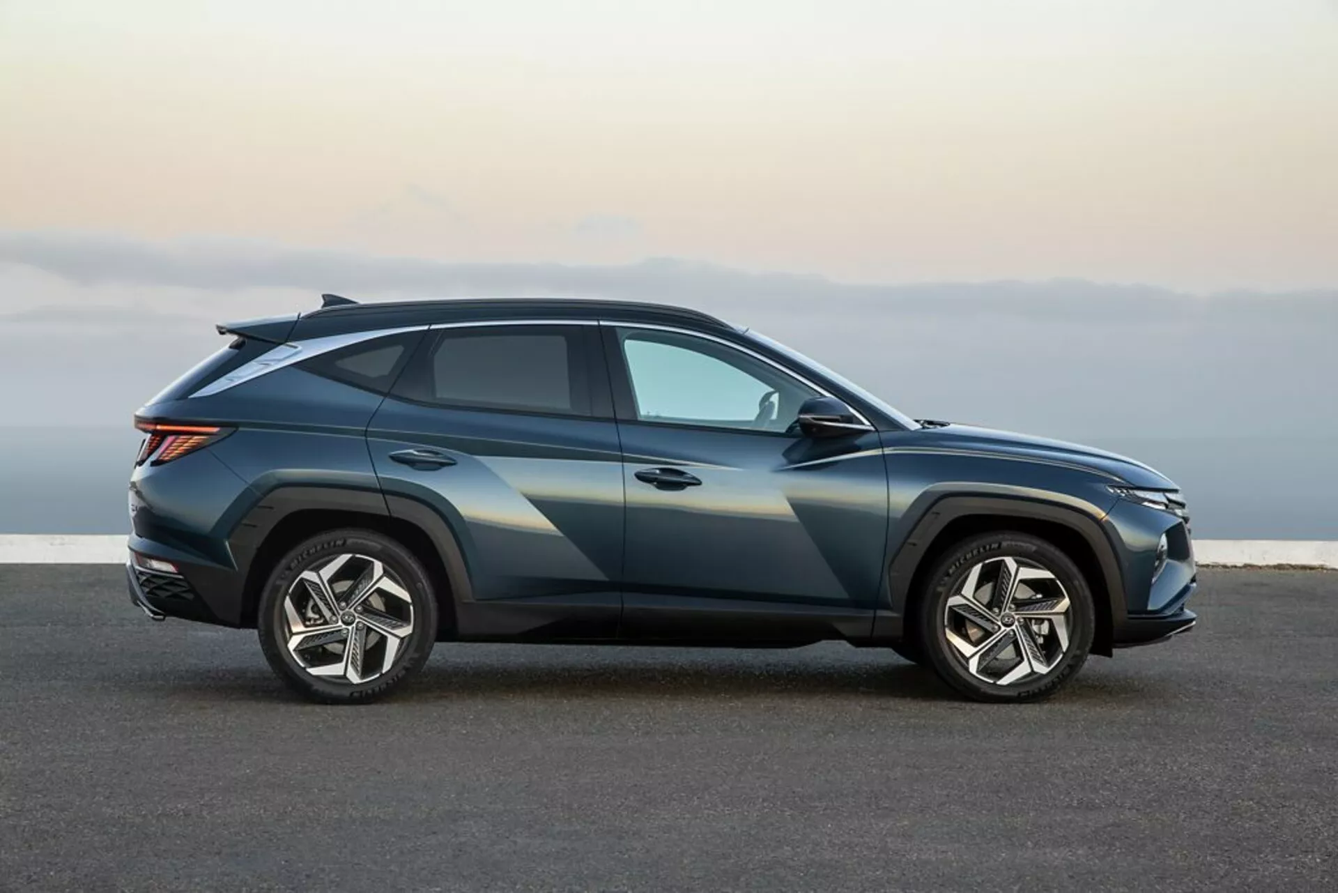Vue de profil du Hyundai Tucson 2020 en bleu métallique foncé avec une ligne de toit sportive façon coupé, grandes jantes en alliage à cinq branches et éclairage avancé, sur une surface d'asphalte indiquant un design épuré et des fonctionnalités technologiques