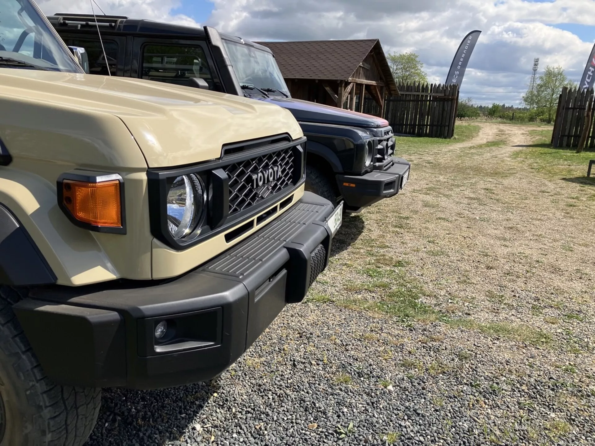 Vue rapprochée et angulaire du côté avant gauche du Toyota FJ Cruiser beige, mettant en évidence la conception robuste du véhicule, les phares carrés, le pare-chocs avant massif avec feux de brouillard intégrés, et le marquage 'TOYOTA' sur la grille proéminente dans un cadre extérieur, possiblement tout-terrain