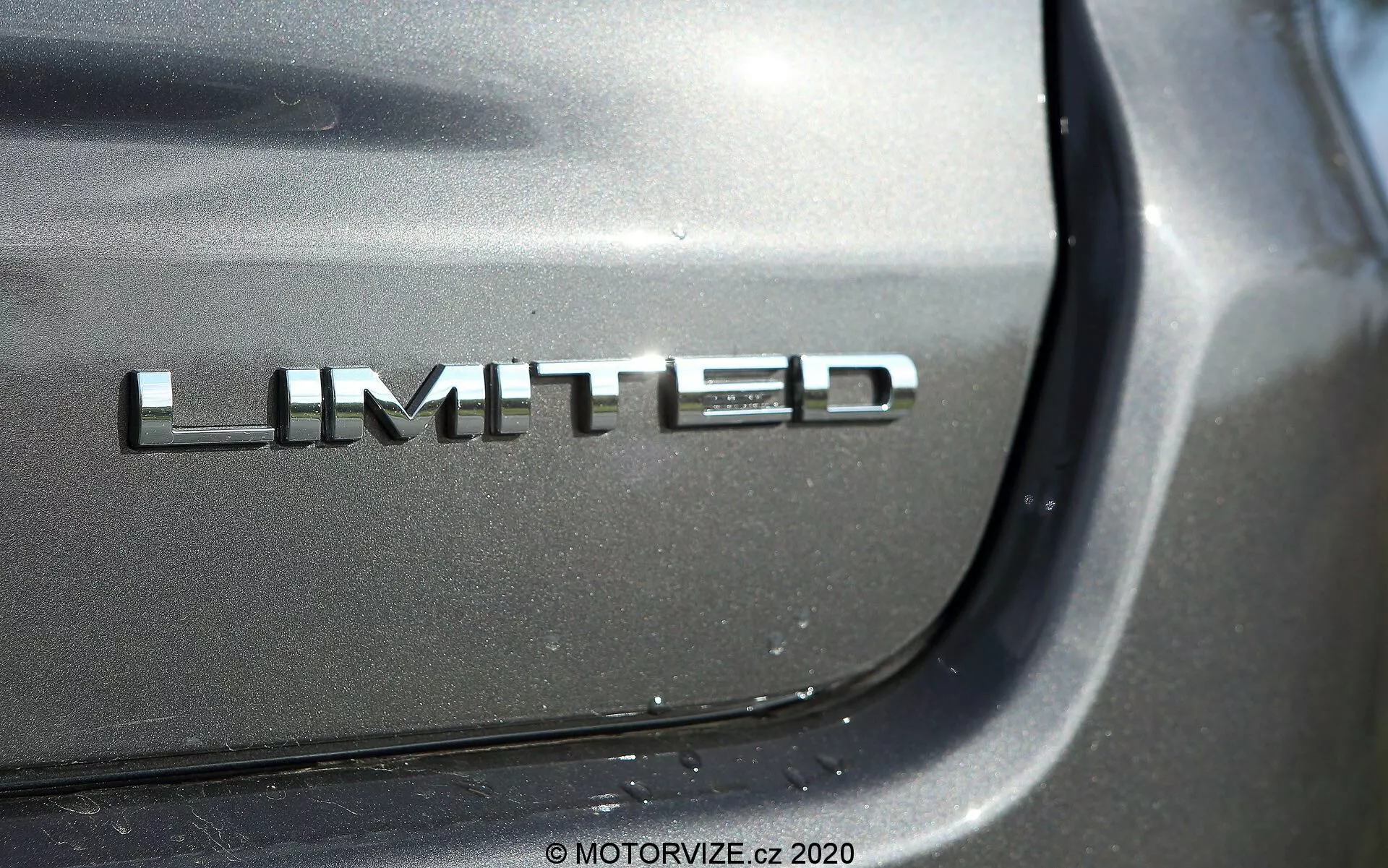 Gros plan sur l'insigne Limited de la Jeep Compass 2017 avec une finition chromée sur le coffre arrière; la photographie met en avant l'insigne sous un angle avec un reflet éclatant par la lumière directe, floutant les détails environnants de la voiture pour souligner la peinture métallique de haute qualité.