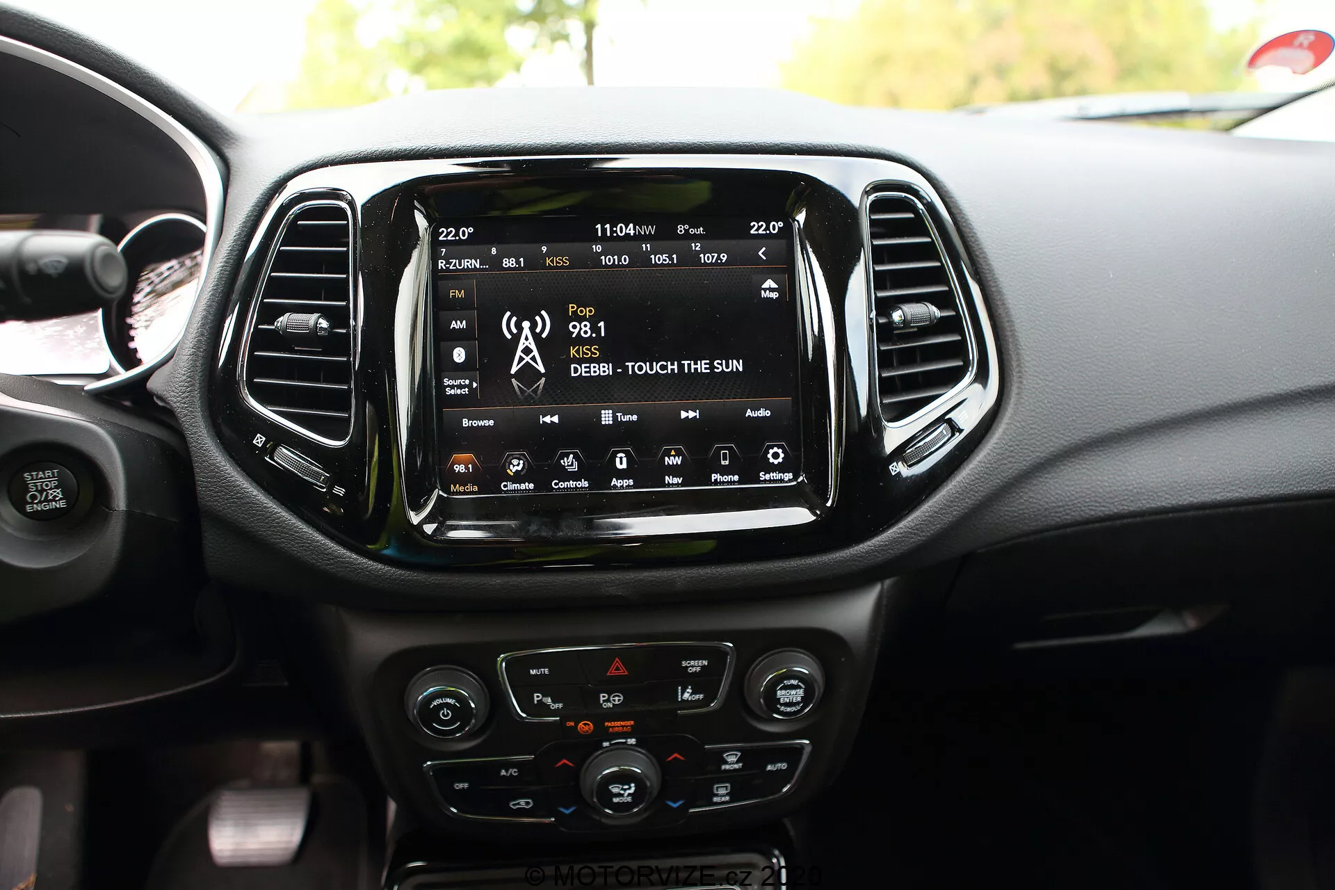 L'intérieur d'une Jeep Compass 2017, mettant en avant la zone centrale du tableau de bord avec un grand écran tactile central d'infodivertissement affichant des fonctionnalités de connectivité telles que la radio, les médias et la navigation par satellite. Sous l'écran tactile se trouvent les commandes du système de climatisation, comprenant des cadrans et des boutons avec des accents chromés et un affichage LCD. Les commandes montées sur le volant partiellement visible incluent des options pour le régulateur de vitesse et le réglage du volume audio. Des détails de conception supplémentaires tels que les bouches d'aération verticales, les commandes de chauffage des sièges et un port USB sont également visibles, mettant en évidence la technologie intérieure et le design esthétique du véhicule.
