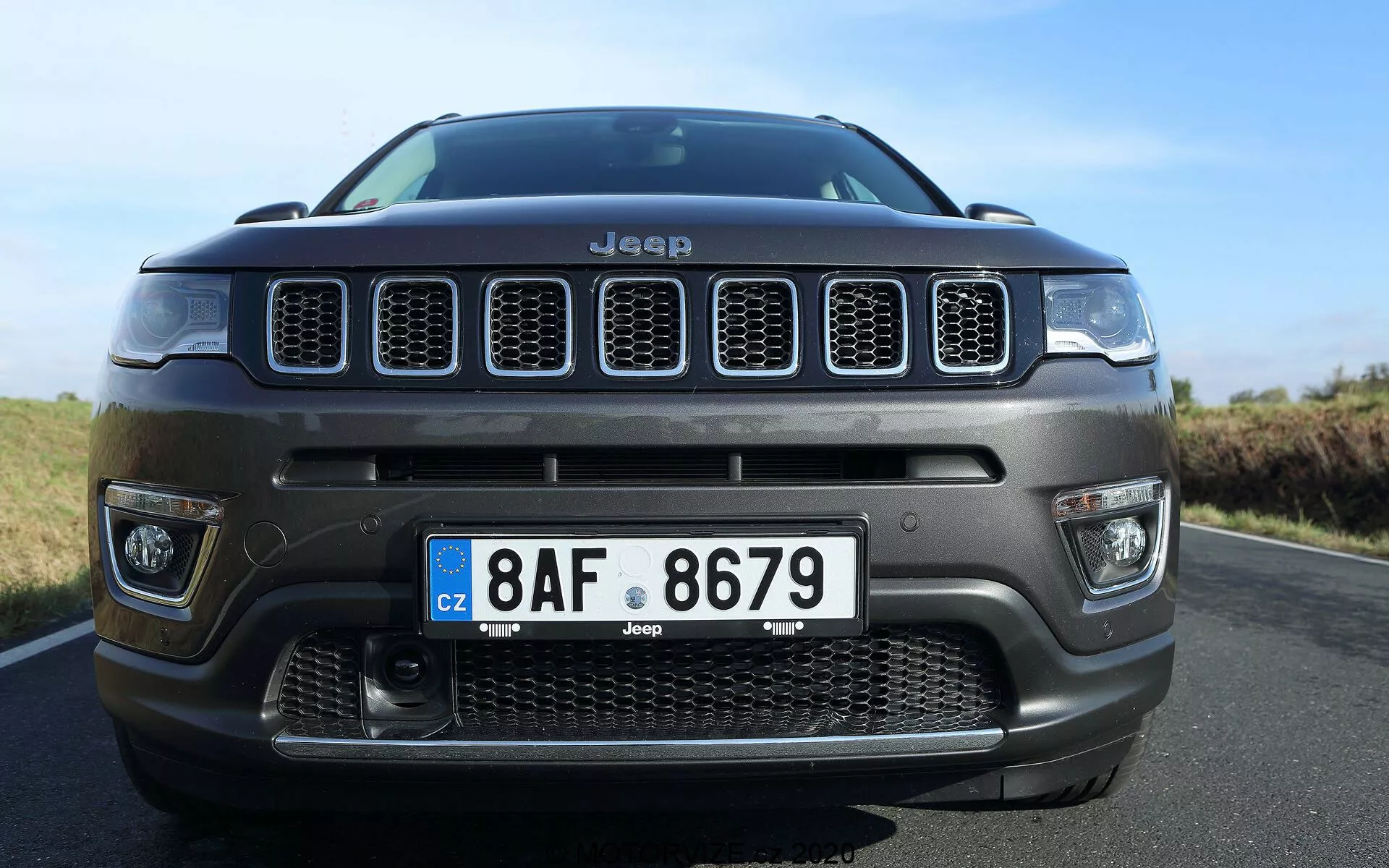 Vue de face en angle bas d'une Jeep Compass 2017, mettant en évidence la grille distinctive à sept fentes et le pare-chocs avant central avec une grande grille d'admission d'air. La photo en gros plan, légèrement décentrée vers la droite, met en avant la posture imposante du véhicule en se concentrant sur la grille, les détails du pare-chocs, la plaque d'immatriculation de style européen et les éléments de design robustes, révélant l'identité et les capacités tout-terrain de la Jeep.