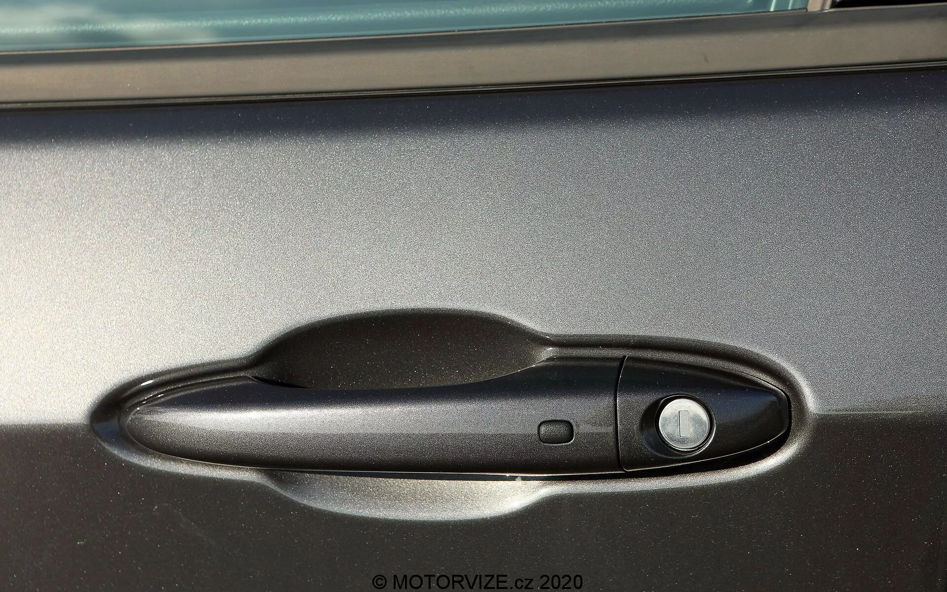 Vue de près latérale de la poignée de porte du Jeep Compass 2017, présentant une poignée noire avec finition mate et bouton d'entrée sans clé, capturée à la lumière naturelle avec garniture métallique visible au-dessus.