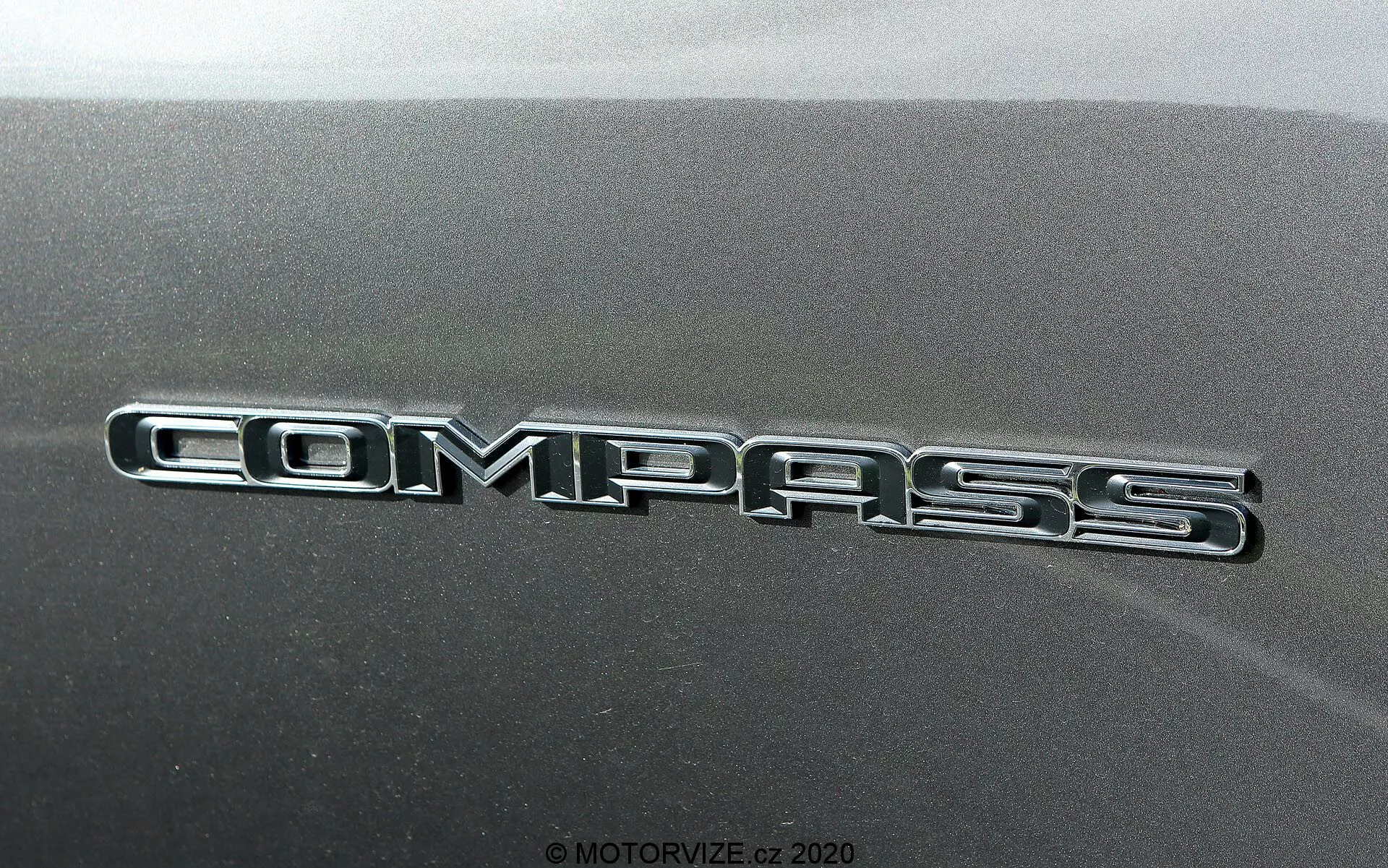 Vue rapprochée du badge du Jeep Compass 2017 avec une inscription chromée brillante sur un panneau de carrosserie texturé.