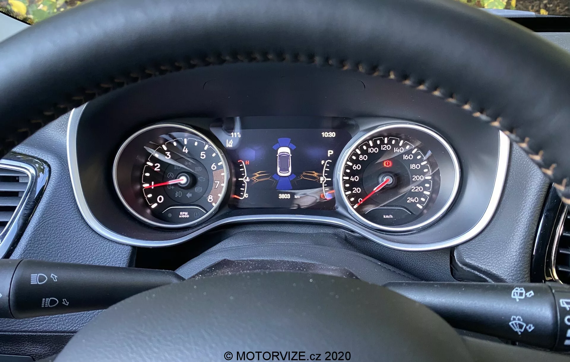 Vue rapprochée du tableau de bord de la Jeep Compass 2017 depuis la perspective du conducteur, mettant en vedette à la fois des jauges analogiques et un écran numérique central. Les caractéristiques comprennent un compte-tours, un compteur de vitesse à double unité, un indicateur de sélection de vitesse, une jauge de carburant, un odomètre et d'autres indicateurs de technologies de sécurité telles que l'assistance au maintien de voie. Les coutures sur le volant en matériau semblable au cuir soulignent des matériaux de qualité et un confort accru, tandis que les manettes de contrôle et les boutons suggèrent des fonctionnalités avancées de commodité et d'assistance au conducteur.