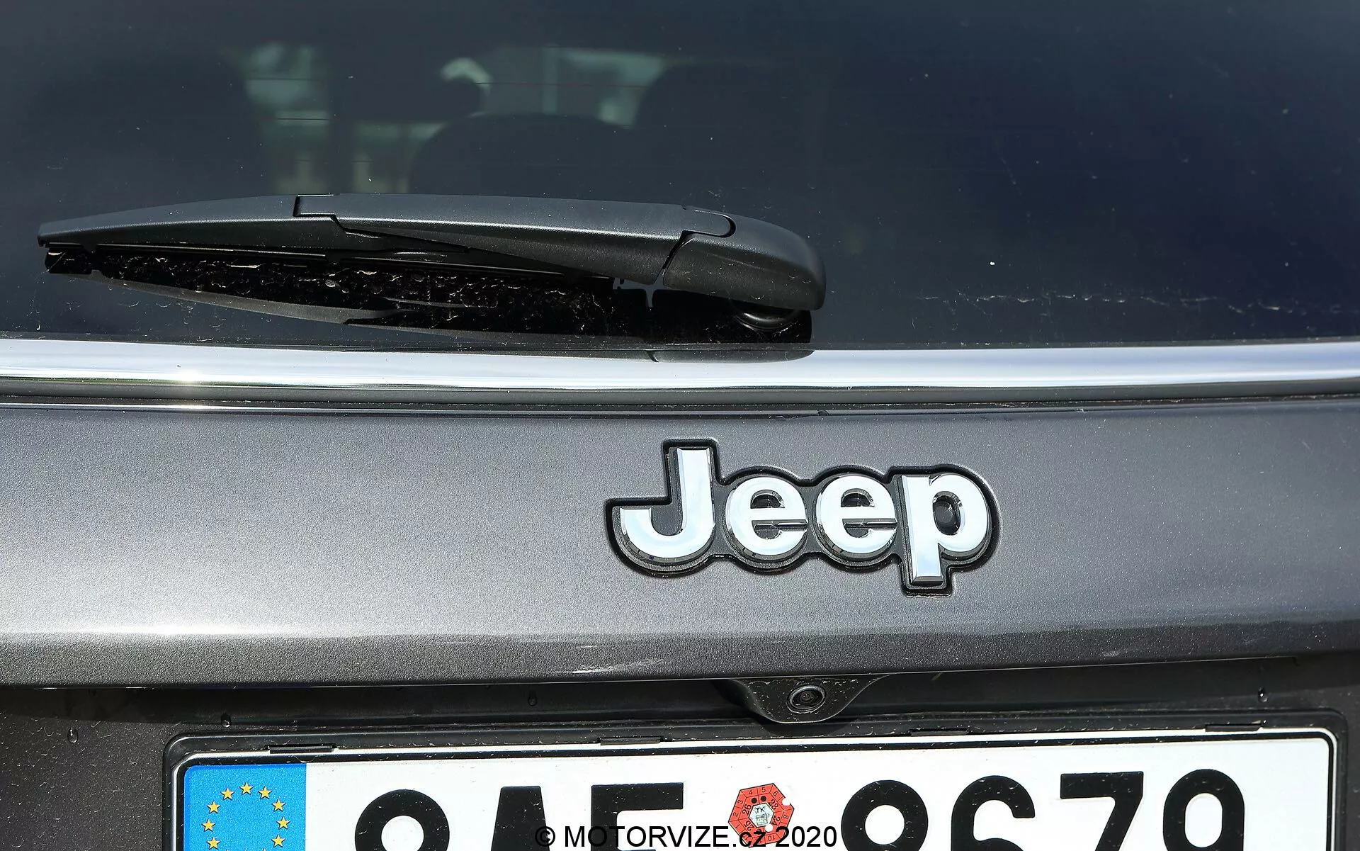 Vue arrière rapprochée d'une Jeep Compass 2017 montrant le logo Jeep centré, l'essuie-glace arrière et une plaque d'immatriculation de style européen partiellement visible avec un identifiant de pays flou