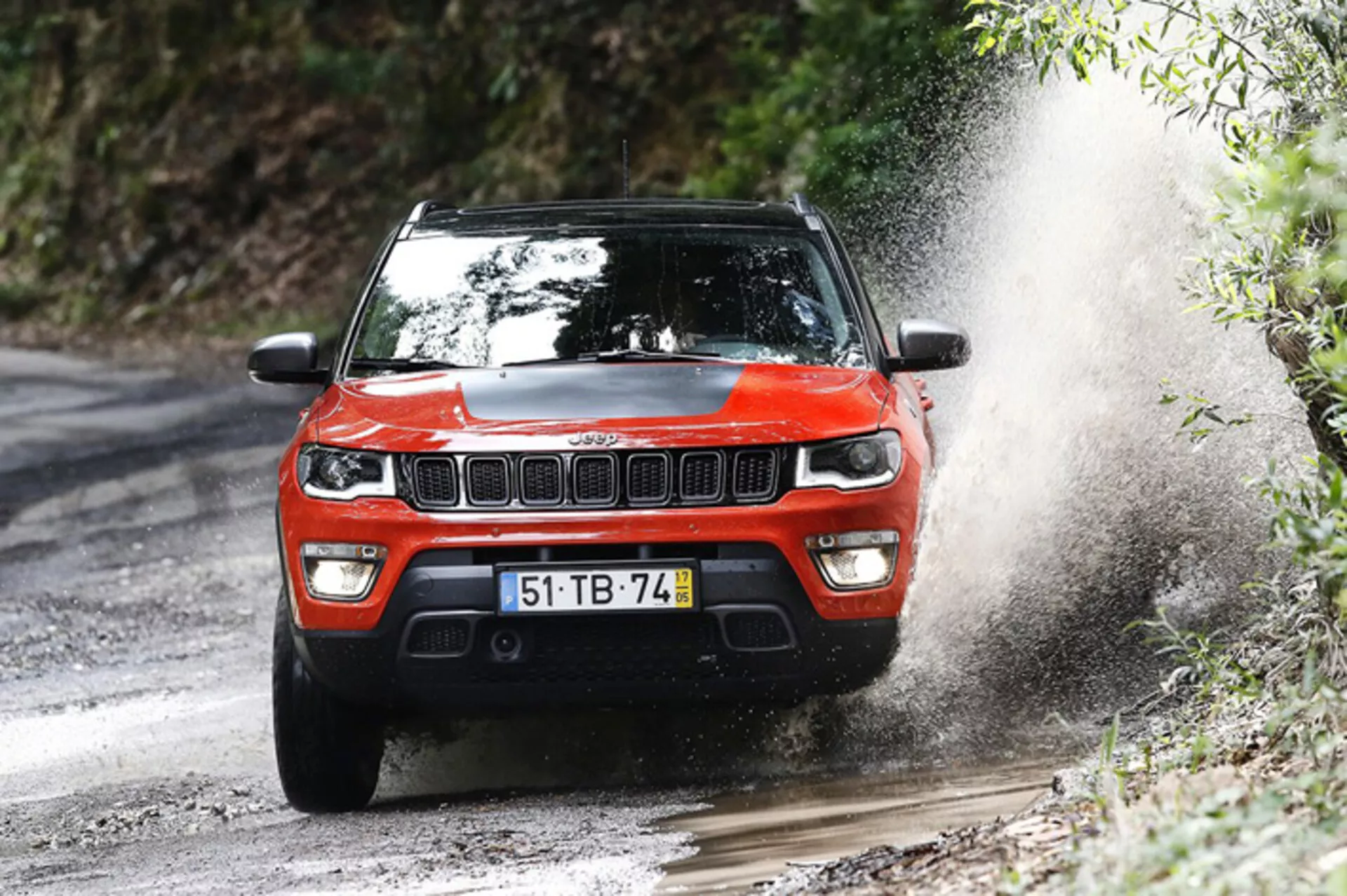 SUV Jeep Compass 2017 en action dynamique tout-terrain, présenté sous un angle avant trois quarts soulignant sa conception robuste et ses capacités de performance sur un chemin forestier boueux.