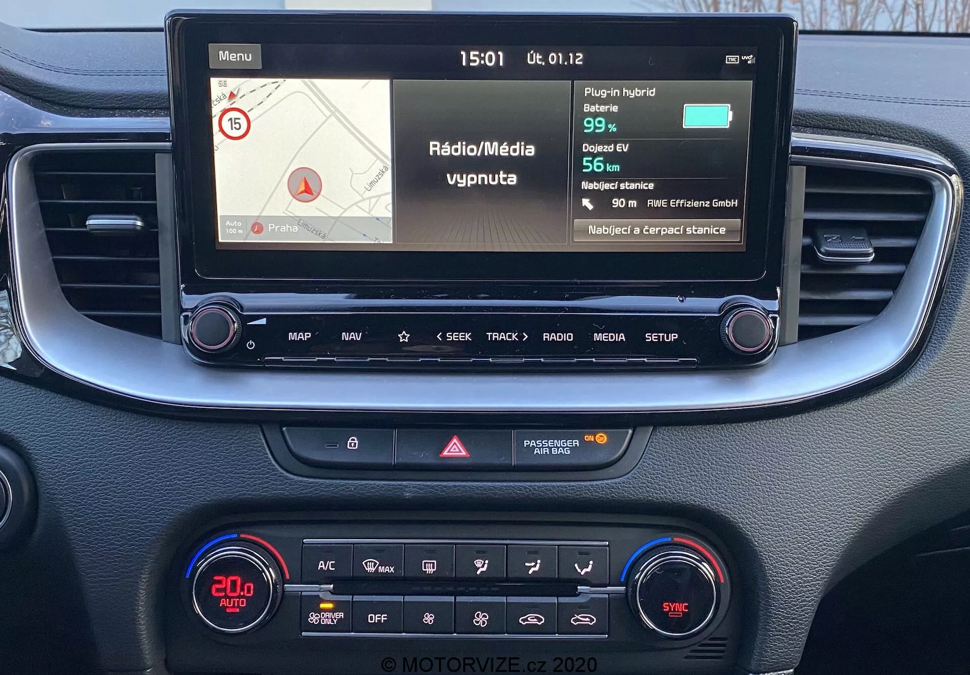 Vue en première personne de la console centrale et du système d'infodivertissement de la Kia Ceed 2018, avec un écran couleur affichant des informations de navigation et de média, des boutons physiques pour le contrôle et un panneau de commande climatique avec affichage numérique et diverses fonctionnalités.