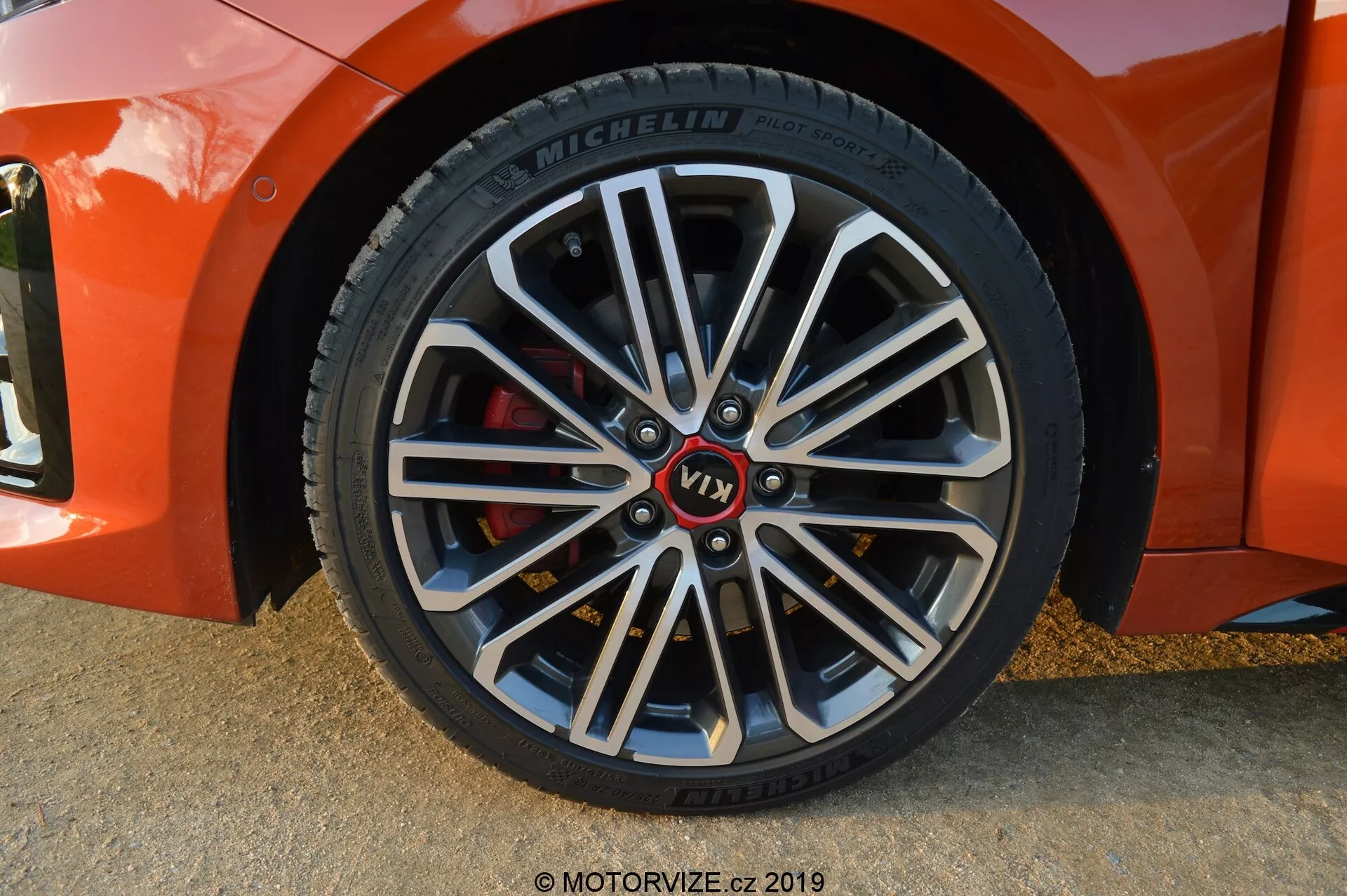 Gros plan sur la roue avant côté passager d'une Kia Ceed 2021, avec un léger angle diagonal, montrant une jante en alliage à plusieurs branches avec des sections internes plus sombres et des bords extérieurs brillants. Présente un moyeu de marque avec une inscription rouge 'VT1', un pneu Michelin avec des informations détaillées sur le flanc et un étrier de frein rouge indiquant des composants orientés vers la performance. Les ombres douces et les reflets suggèrent que la photo a été prise à la lumière naturelle, probablement pendant l'heure dorée.