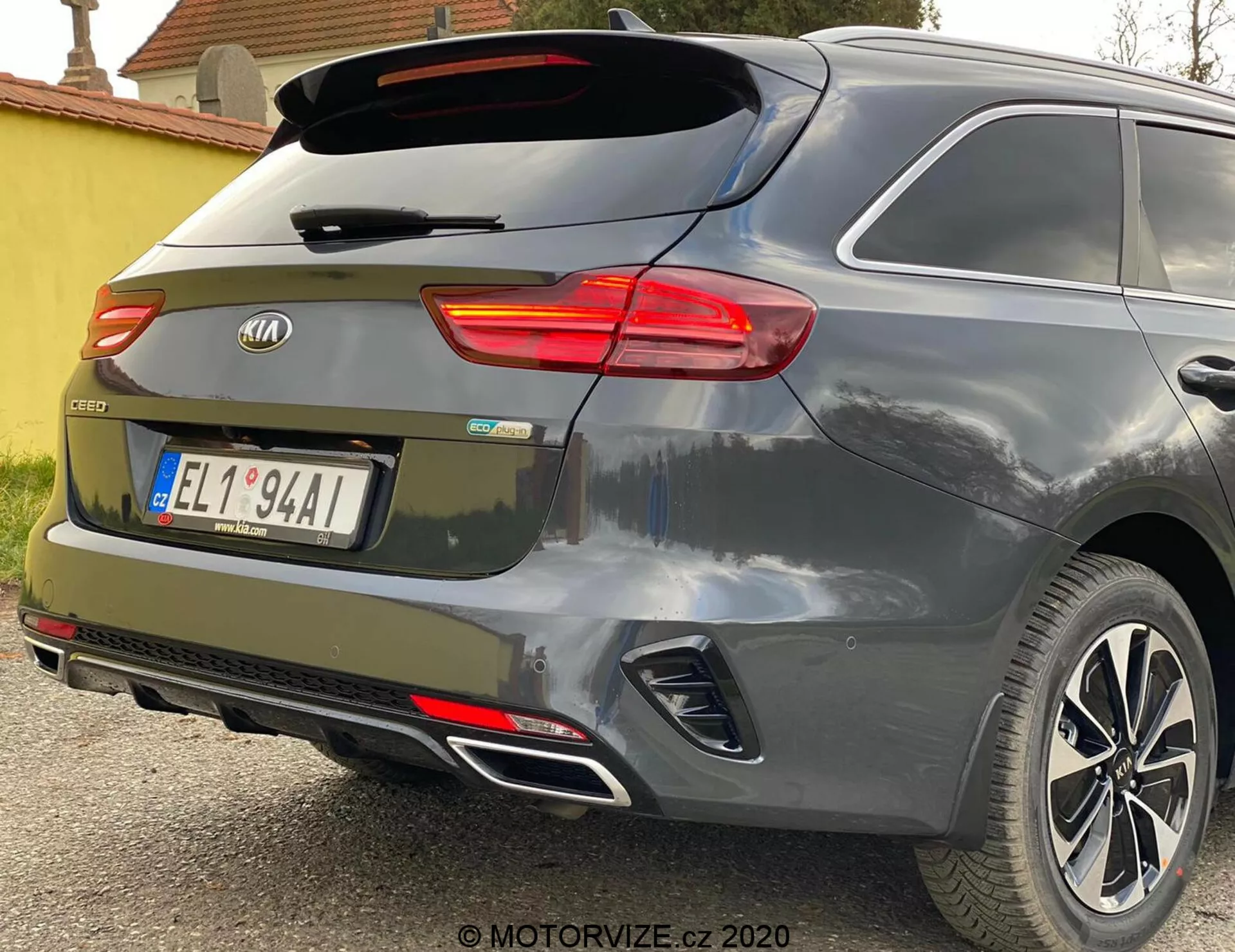 Vue angulaire arrière partielle d'une Kia Ceed 2018, mettant en évidence le feu arrière droit allumé, le pare-brise arrière avec essuie-glace, le hayon avec l'emblème de la marque et le badge du modèle 'CEED', des réflecteurs intégrés dans le pare-chocs arrière, des capteurs de stationnement, un système d'échappement double et des roues en alliage sur une peinture gris métallique ou argent.