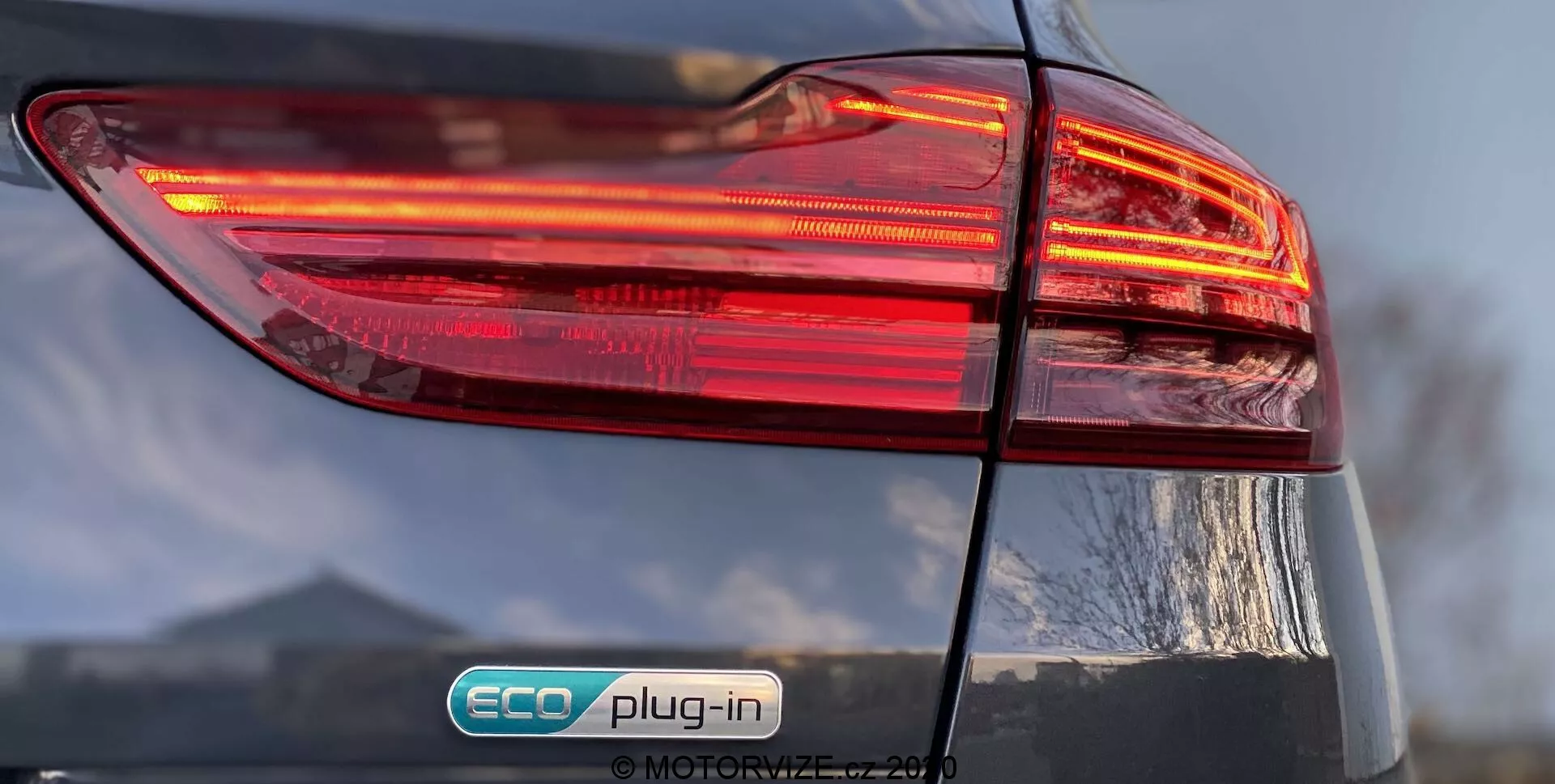 Vue rapprochée du côté arrière gauche d'une Kia Ceed 2018, se concentrant sur le bloc de feux arrière illuminé avec un design multicouches. Le badge 'ECO plug-in' indique qu'il s'agit d'un véhicule hybride rechargeable. La finition brillante et le couvercle du coffre légèrement visible ajoutent des détails au design global de la voiture.