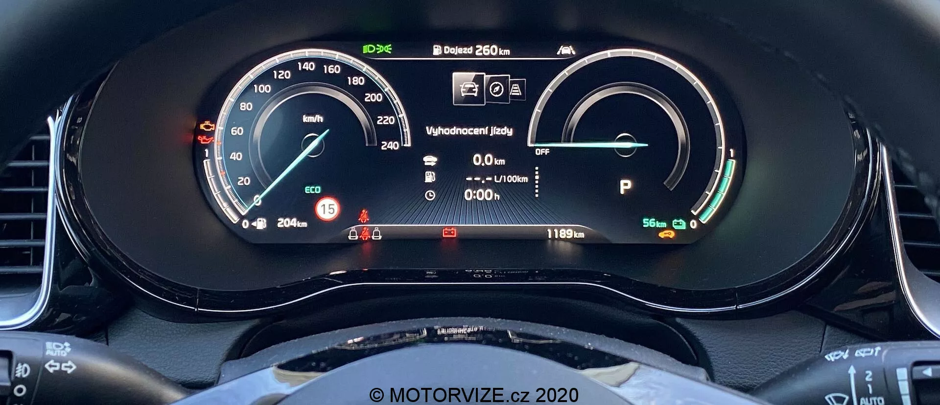 Vue rapprochée du tableau de bord numérique du Kia Ceed 2018 prise depuis le siège du conducteur. L'affichage comprend un compteur de vitesse avec une aiguille physique et une lecture numérique indiquant 15 km/h. À droite, il y a un indicateur de puissance/batterie montrant une batterie pleine avec une autonomie de 481 km. D'autres éléments incluent un écran de statut prêt, des informations conducteur avec des voyants d'alerte, une lecture de température extérieure de 20,5°C et le véhicule en mode Park. L'arc supérieur du volant est visible, avec un design sportif à fond plat.