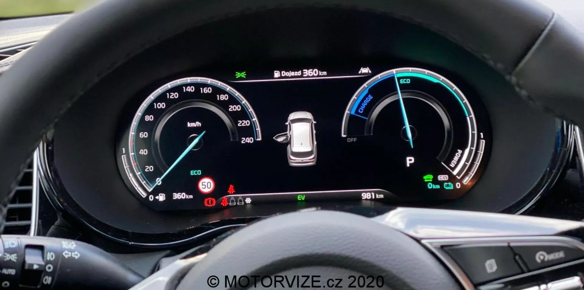 Vue rapprochée du tableau de bord numérique de la Kia Ceed 2018 depuis la perspective du conducteur, avec un grand écran panoramique et une instrumentation détaillée incluant un tachymètre jusqu'à 260 km/h, un indicateur de puissance avec les modes Éco, Confort et Puissance, un avertissement de pression des pneus et un indicateur de mode 'Park'. Le tableau de bord affiche également un système de caméras à 360 degrés et un odomètre marquant 9811 km. Le bord entourant réduit les reflets et les boutons du volant sont partiellement visibles. Filigrane 'MOTORVIZE.cz 2020'.