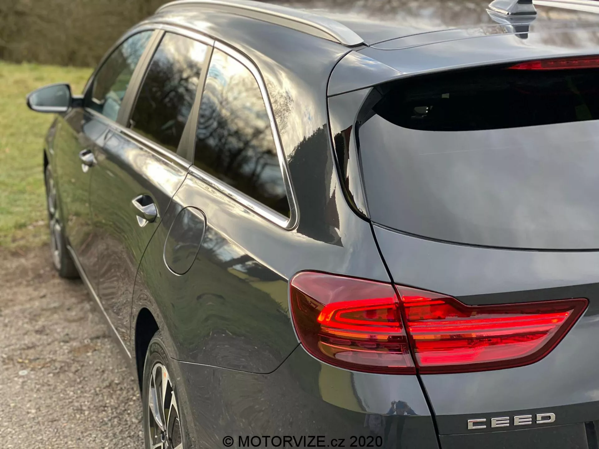 Vue partielle latérale et arrière d'une moderne voiture berline grise Kia Ceed 2018 mettant en valeur le feu arrière LED en forme de C illuminé, design de berline avec essuie-glace arrière et subtil spoiler de toit, antenne en forme d'aileron de requin, roues en alliage et badge de la marque avec le nom du modèle 'CEED', capturée sous la lumière naturelle de fin d'après-midi et une faible profondeur de champ se concentrant sur le véhicule.