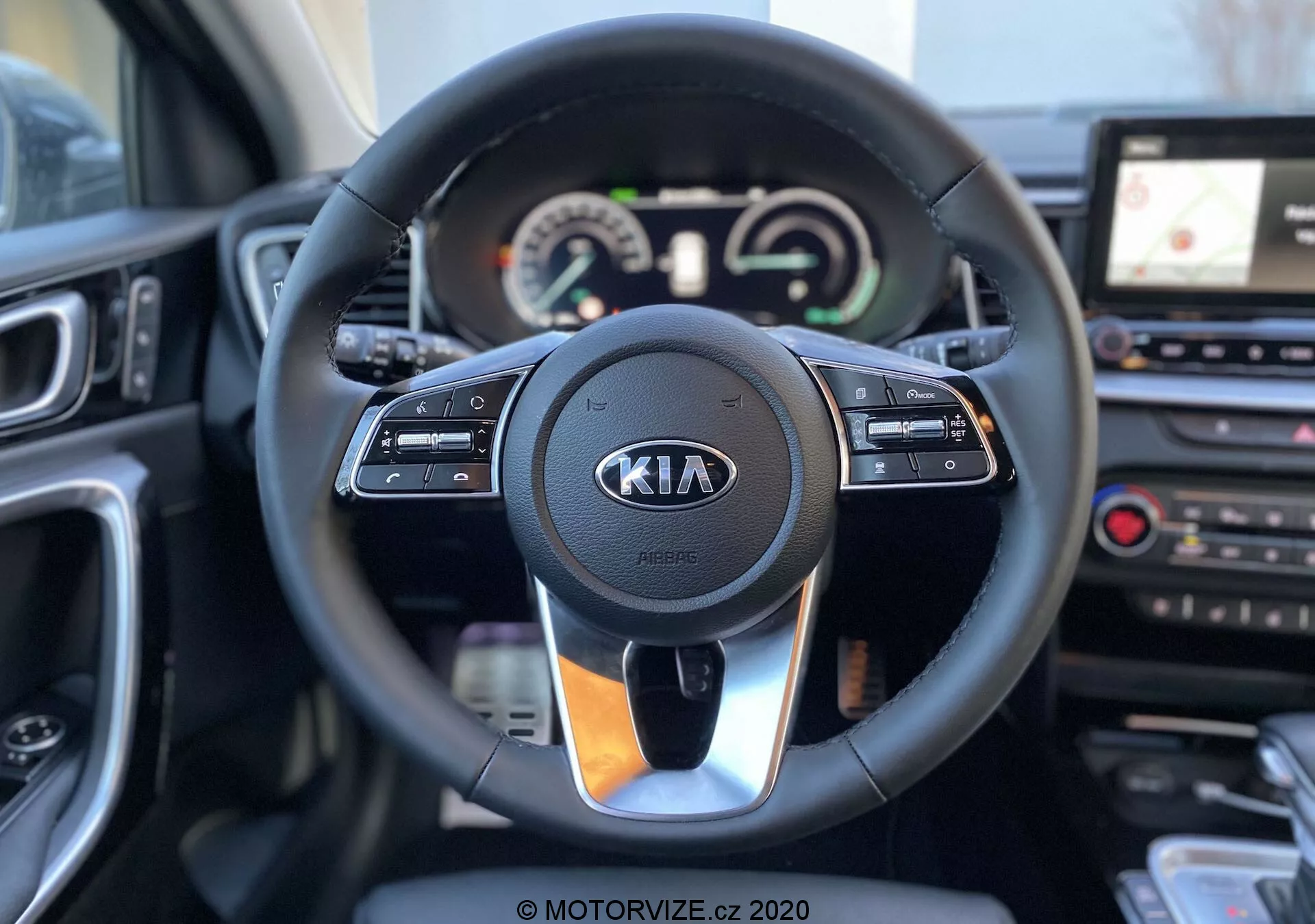 Vue intérieure d'une Kia Ceed 2018, centrée sur le volant et le tableau de bord depuis la perspective du siège conducteur. Le volant moderne dispose de commandes intégrées pour le régulateur de vitesse, l'interaction multimédia et la communication mains libres, avec le logo Kia bien visible. Derrière le volant, un groupe d'instruments combine des cadrans analogiques et un écran digital affichant les lectures du compteur de vitesse et du tachymètre, ainsi qu'un écran multifonctionnel. À droite du volant, une partie de la console centrale est visible, avec un système d'infodivertissement à écran tactile et la navigation GPS, ainsi que des commandes de contrôle de la climatisation. L'image est nette, avec une faible profondeur de champ qui met en évidence le volant et ses environs immédiats.