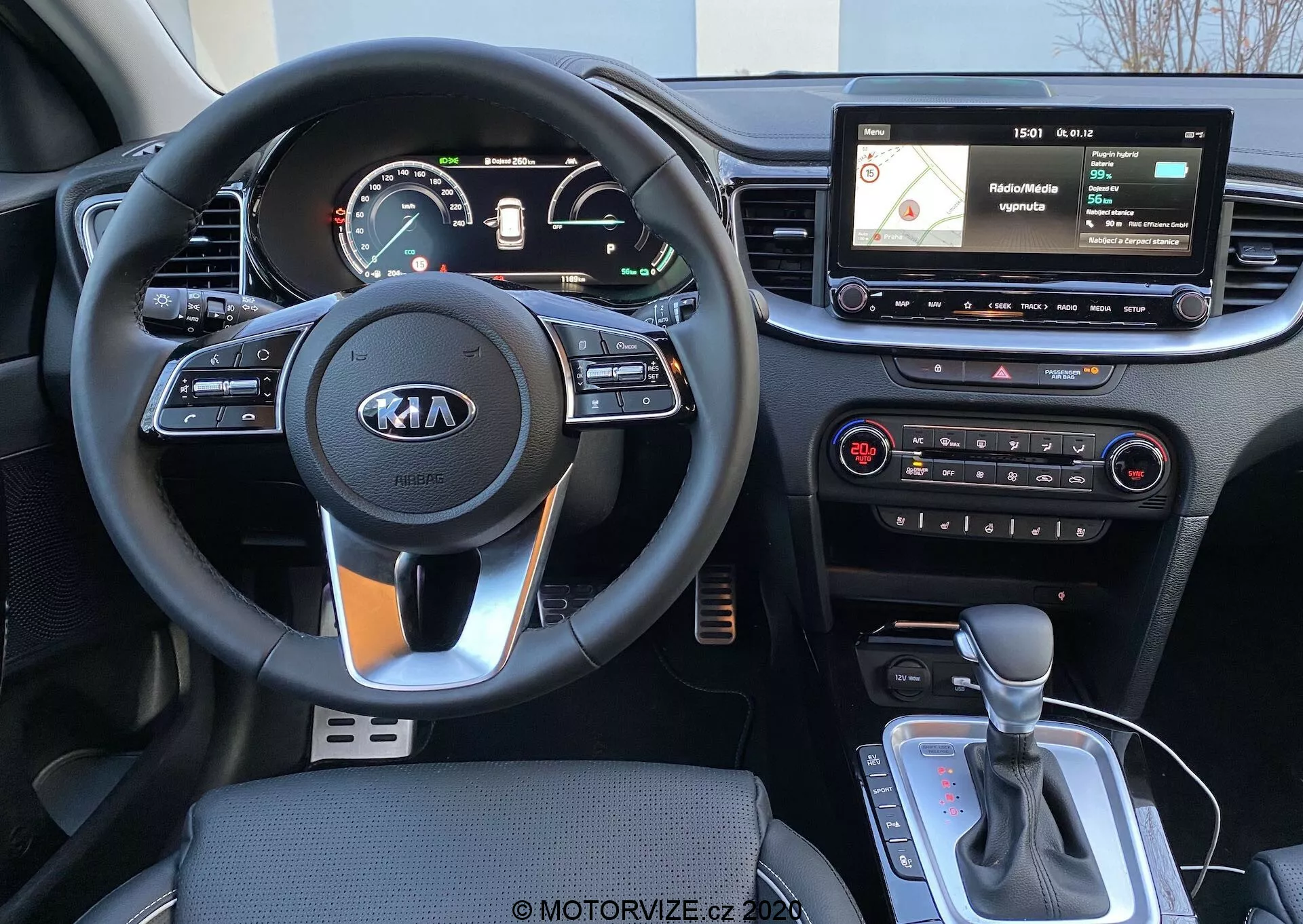 Vue intérieure d'une Kia Ceed 2018 depuis la perspective du conducteur, montrant un volant à trois branches avec le logo Kia, des commandes intégrées au volant, un tableau de bord mixte analogique et numérique, un écran d'info-divertissement flottant avec navigation et interface multimédia, des commandes physiques du système de climatisation et un levier de changement de vitesse automatique avec un éventuel sélecteur de mode de conduite ou frein de stationnement électronique.
