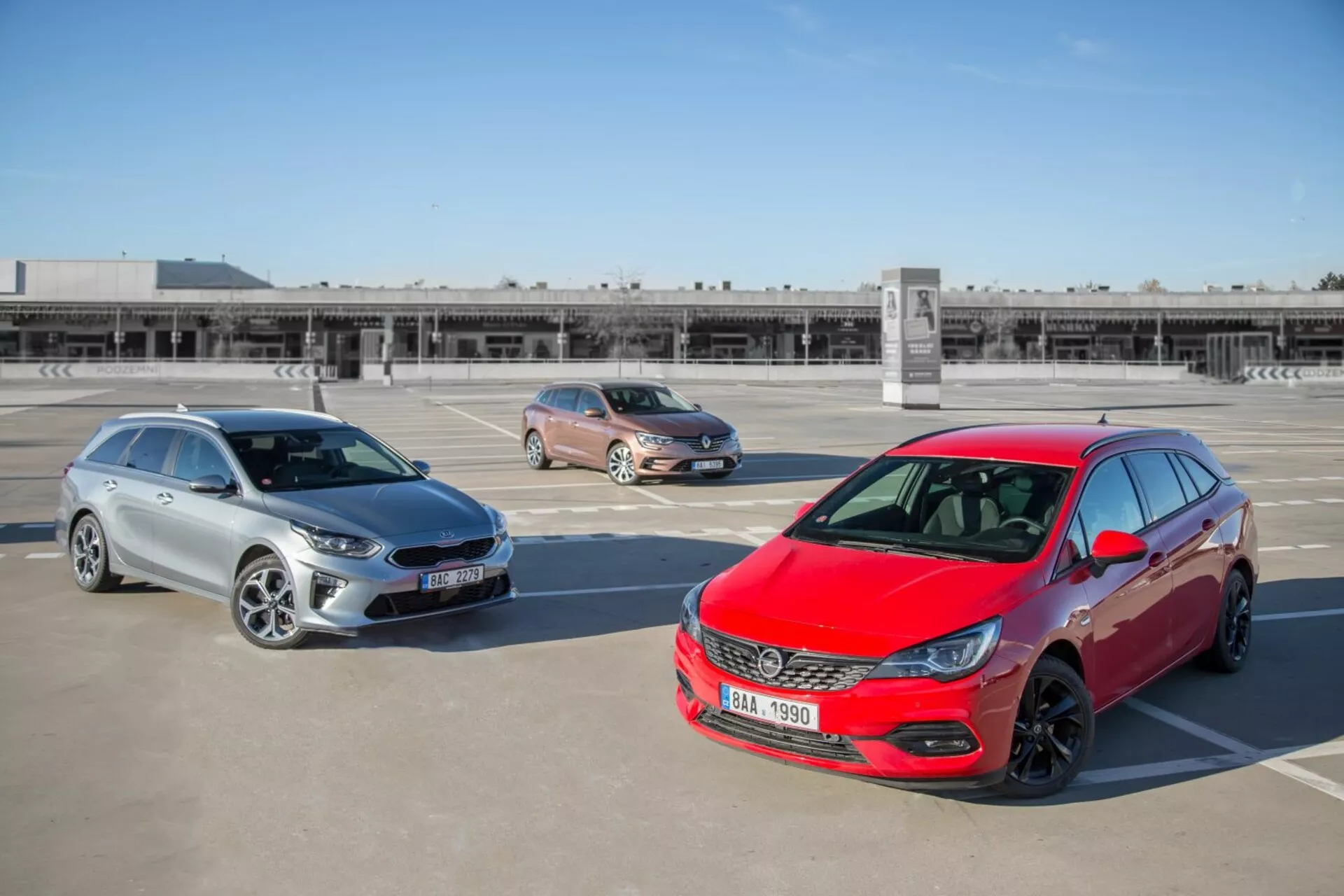 Trois modèles Kia Ceed de 2009 comprenant une hatchback rouge, un crossover doré et un break argenté garés sur un parking en toit-terrasse, photographiés depuis une position surélevée mettant en avant le design de l'avant, les profils latéraux et la longueur des véhicules