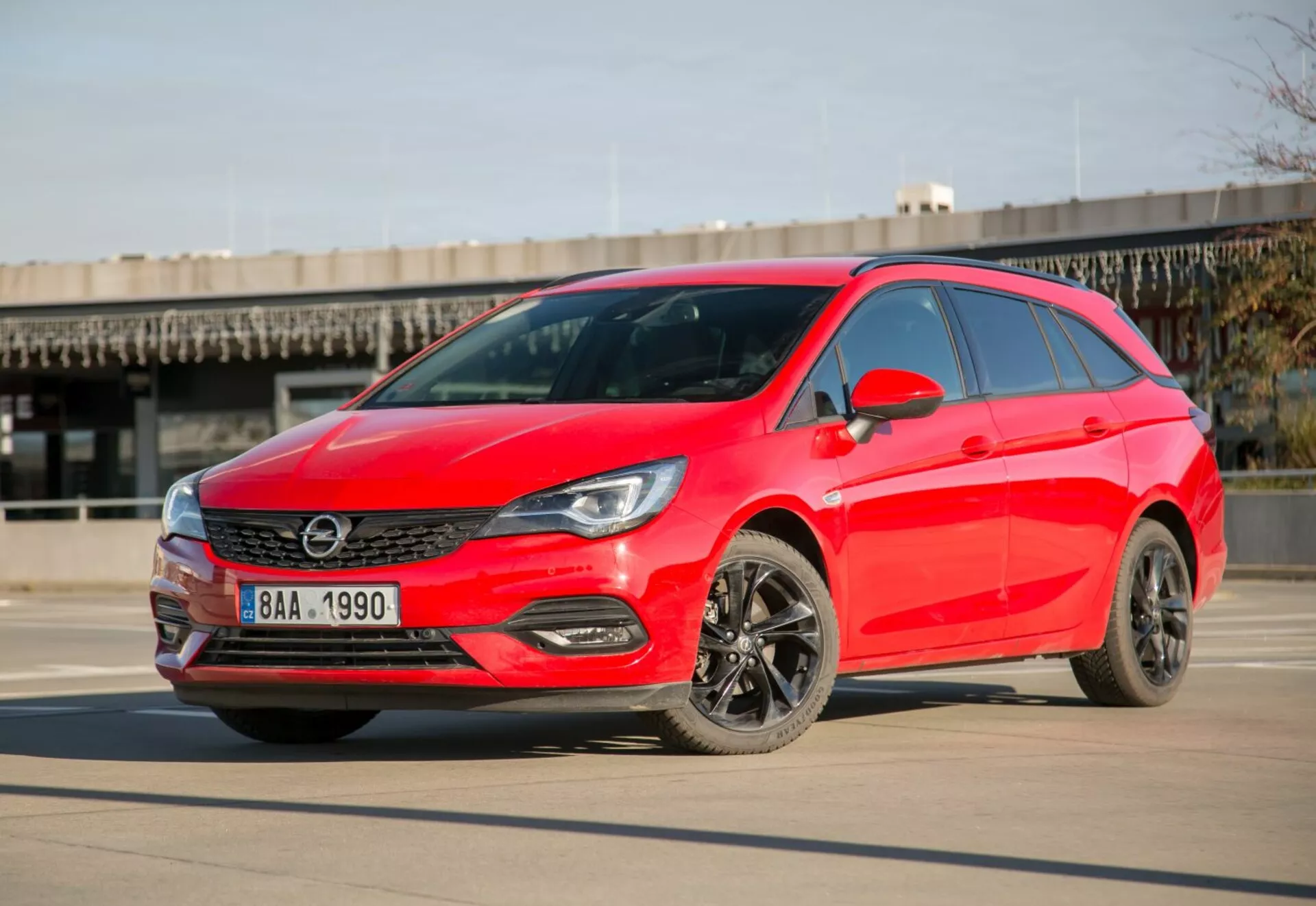 Hatchback Kia Ceed rouge vif de 2009 garée sur du béton lisse sous un ciel clair, montrant des phares LED, une grille élégante, des roues en alliage foncé et un design aérodynamique moderne depuis un angle avant de trois quarts pendant la journée.