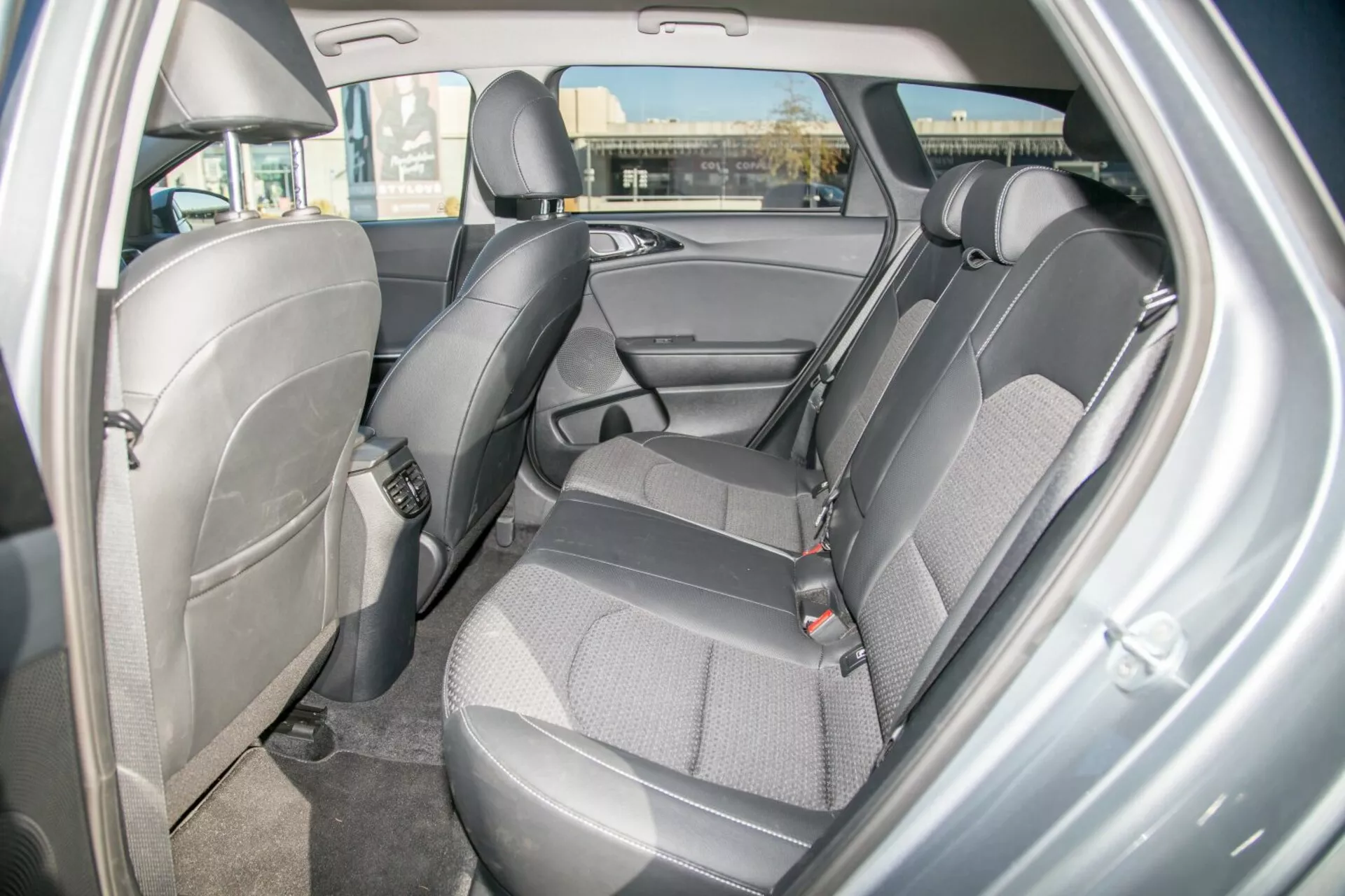 Vue intérieure d'une Kia Cee'd 2009 illustrant la conception et les caractéristiques de l'espace des sièges arrières, mettant en évidence une sellerie en tissu durable bicolore, des ceintures de sécurité visibles, des appuie-têtes réglables, un panneau de porte avec compartiment de rangement, des ancres potentiels pour siège enfant, un sol moquetté et un éclairage dôme ambiant du point de vue de la porte passager arrière côté droit.