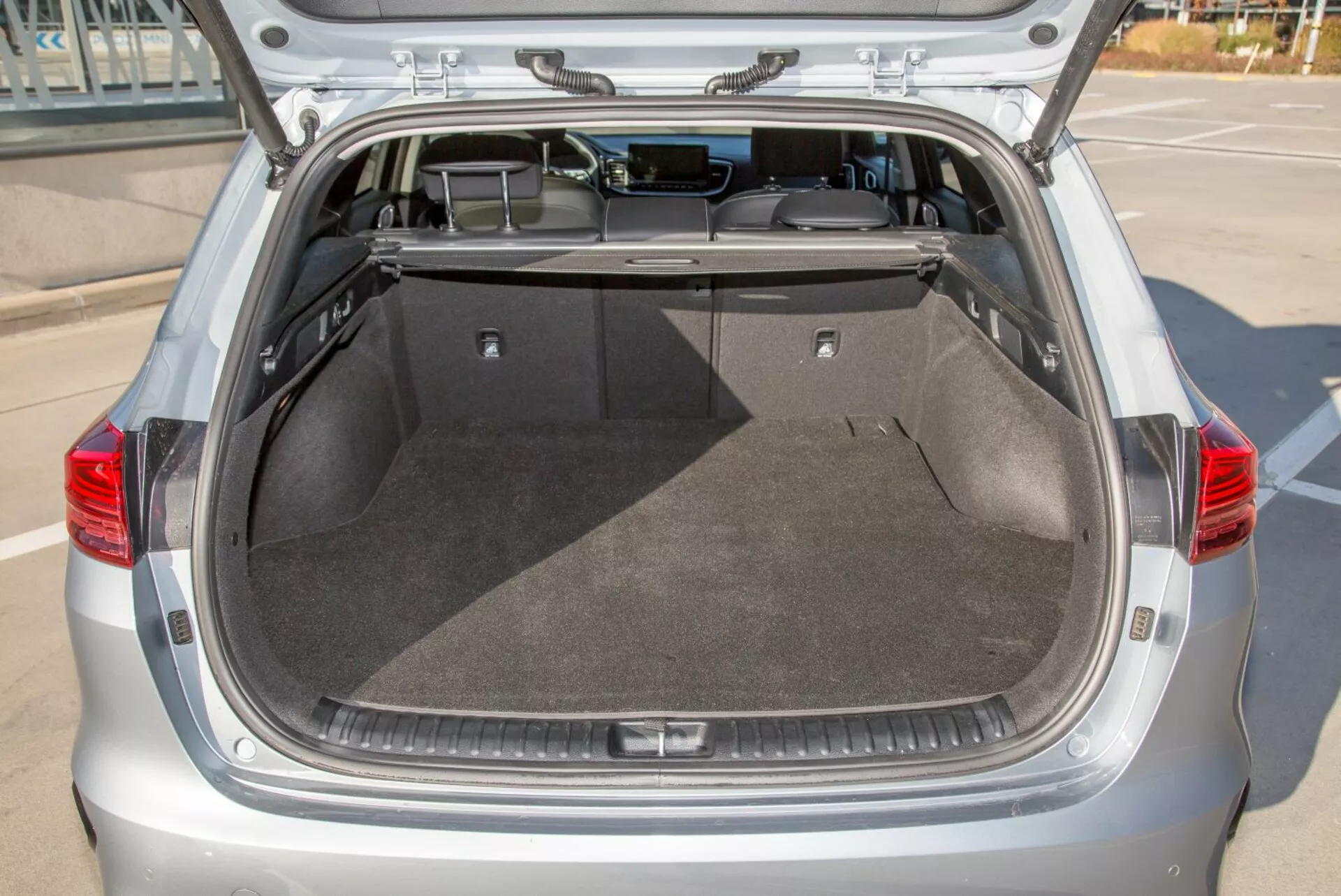 Compartiment du coffre arrière d'une hatchback Kia Cee'd 2009 avec le hayon ouvert, montrant un espace de chargement spacieux et propre, tapisserie, couverture rétractable et éclairage intérieur potentiel