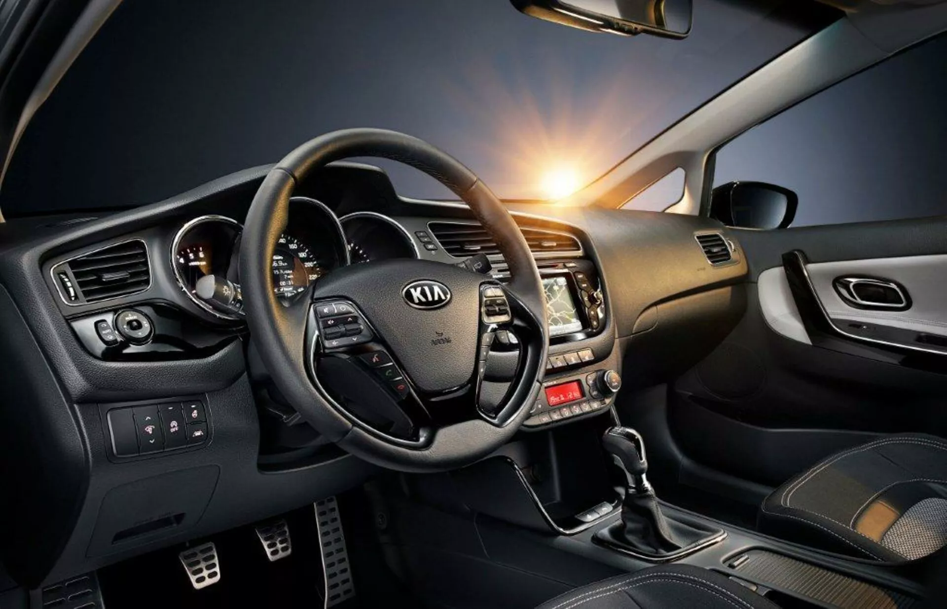 Vue de l'intérieur du cockpit d'une Kia Ceed 2009 mettant en évidence le volant avec commandes intégrées, le tableau de bord accentué de métal et le côté conducteur riche en technologie, y compris le levier de vitesse, les commandes des vitres électriques et l'éclairage d'ambiance.