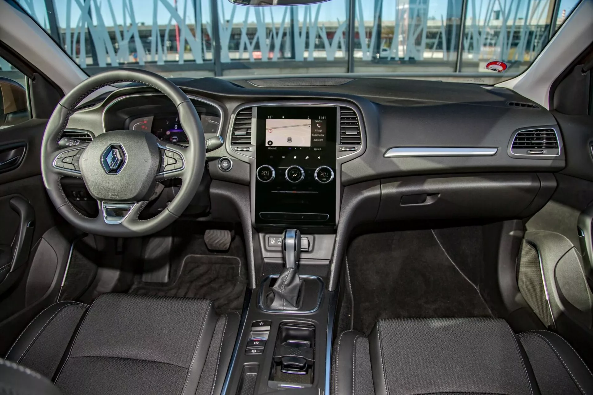 Vue intérieure de la Kia Cee'd 2009 depuis le siège arrière montrant le volant multifonctionnel, le système d'infodivertissement tactile, le levier de vitesses automatique et l'habillage détaillé dans la zone du cockpit avant