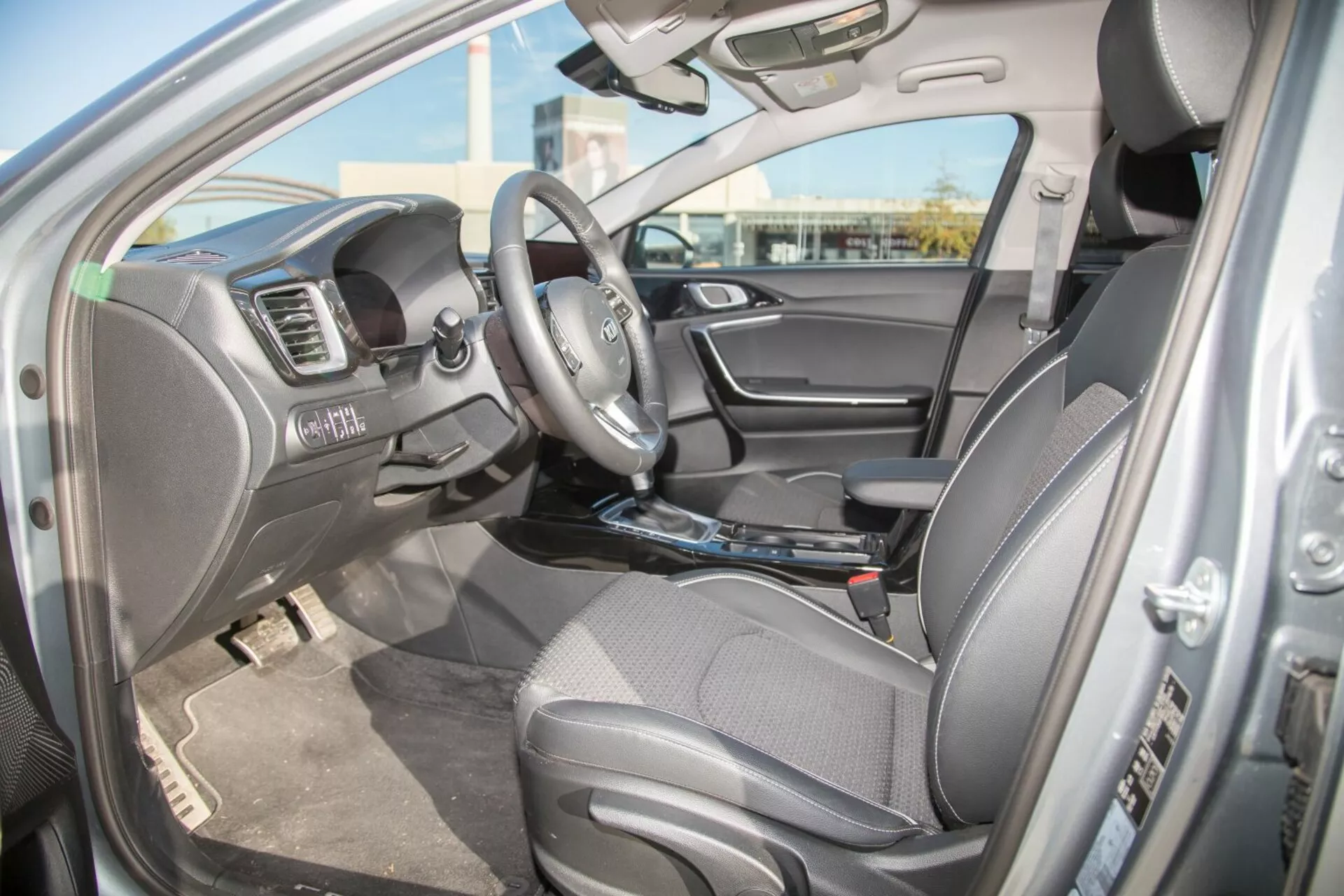 Vue intérieure du Kia Cee'd 2009 côté conducteur montrant le siège, le volant avec commandes intégrées et les fonctionnalités du tableau de bord incluant le système multimédia