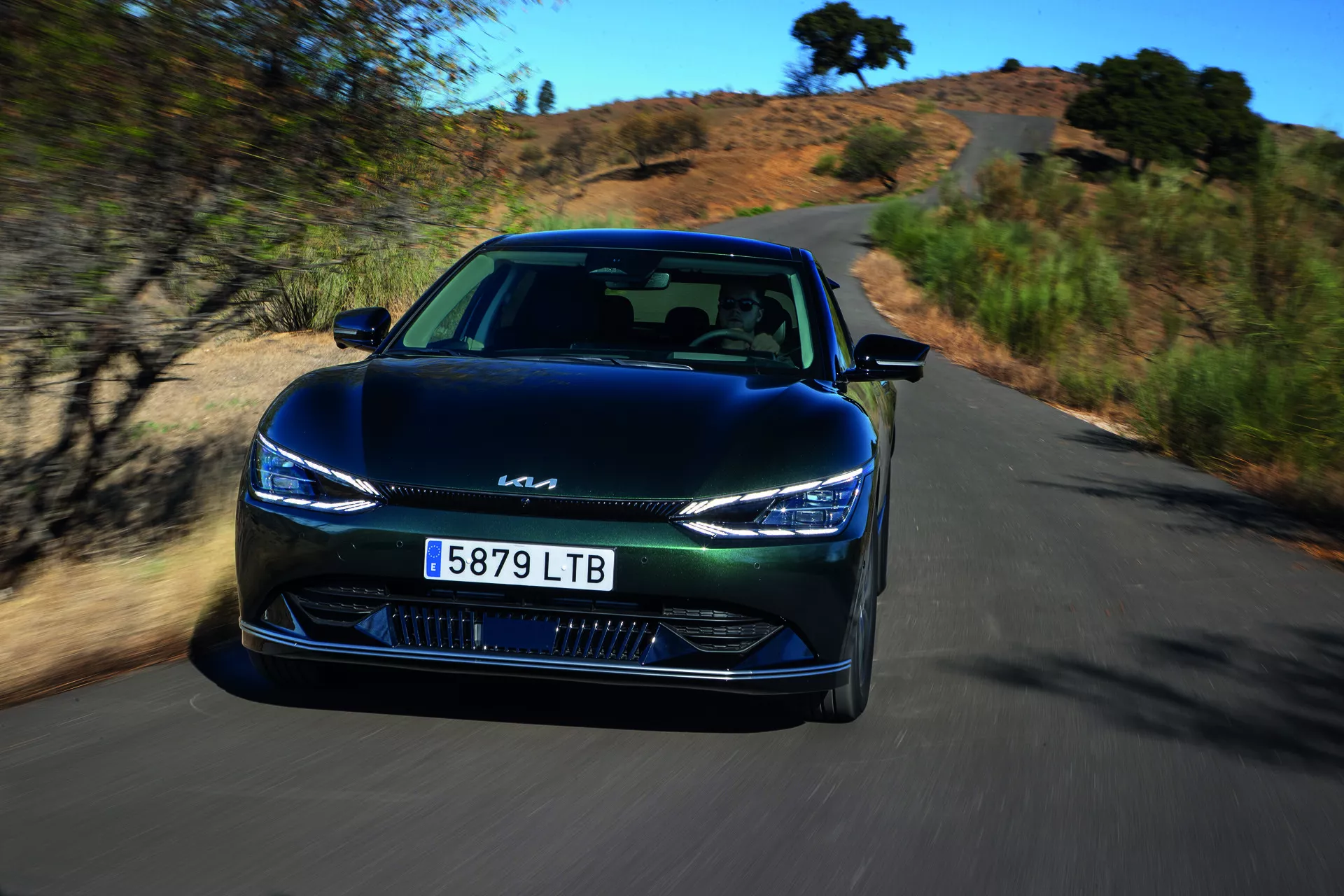 Kia EV6 2021 en mouvement dynamique, vue d'angle avant mettant en évidence des phares LED élégants, un design de grille fermée et une technologie avancée d'assistance au conducteur sur une route scénique naturelle