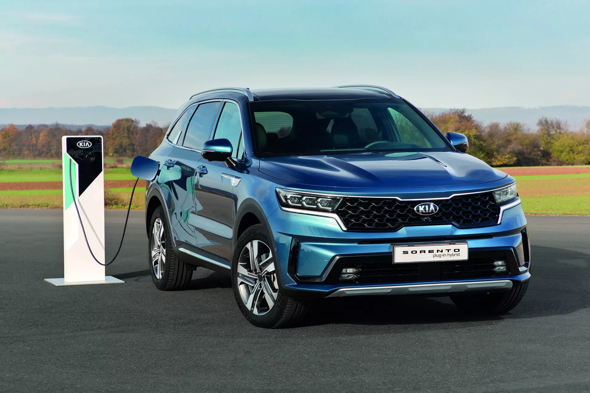 SUV Kia Sorento 2020 bleu, doté de phares LED et de la technologie hybride rechargeable, garé à l'extérieur avec une station de charge en plein jour mettant en valeur son design et ses capacités éco-responsables
