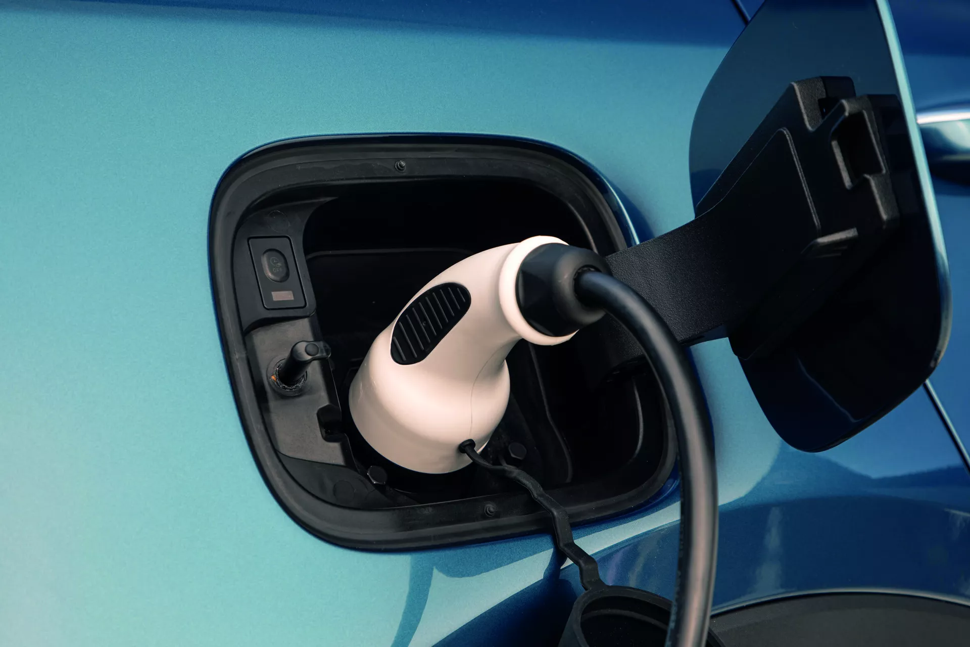 Vue rapprochée de la zone du port de charge sur une Kia Sorento MQ4 2020 en bleu métallique, montrant le connecteur Mennekes de type 2 inséré, soulignant la technologie de recharge de véhicule électrique et la conception du port.