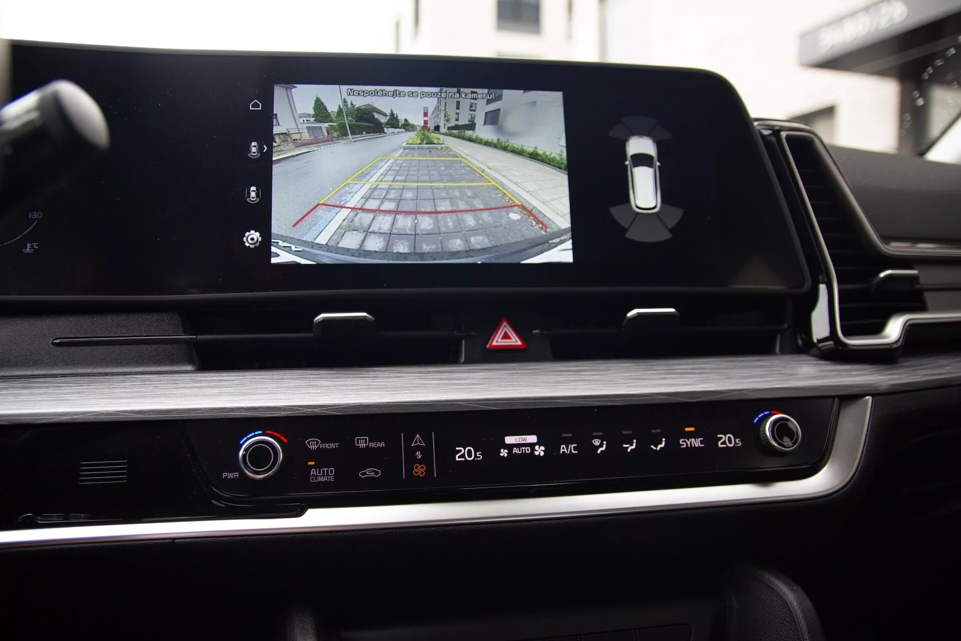 Vue intérieure du Kia Sportage 2022 depuis le siège du conducteur mettant en avant l'écran tactile de l'infodivertissement avec sortie de la caméra de recul, le panneau de contrôle du climatiseur et un design esthétiquement plaisant avec des accents chromés et des finitions brillantes