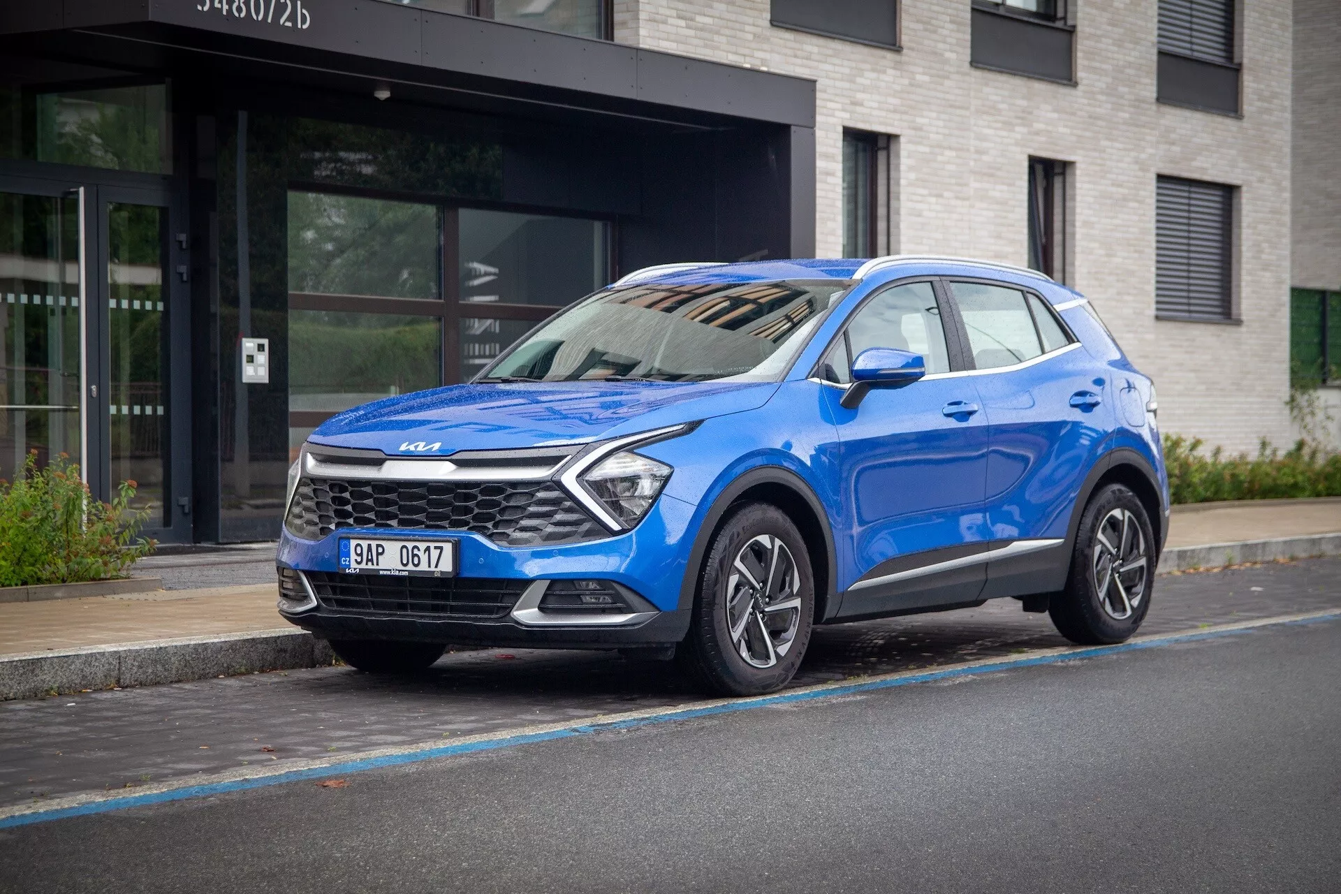 Kia Sportage 2022 en bleu, vue frontale trois-quarts sur une rue urbaine, mettant en évidence sa haute tenue de route, phares LED, jantes alliage et technologie de sécurité moderne.