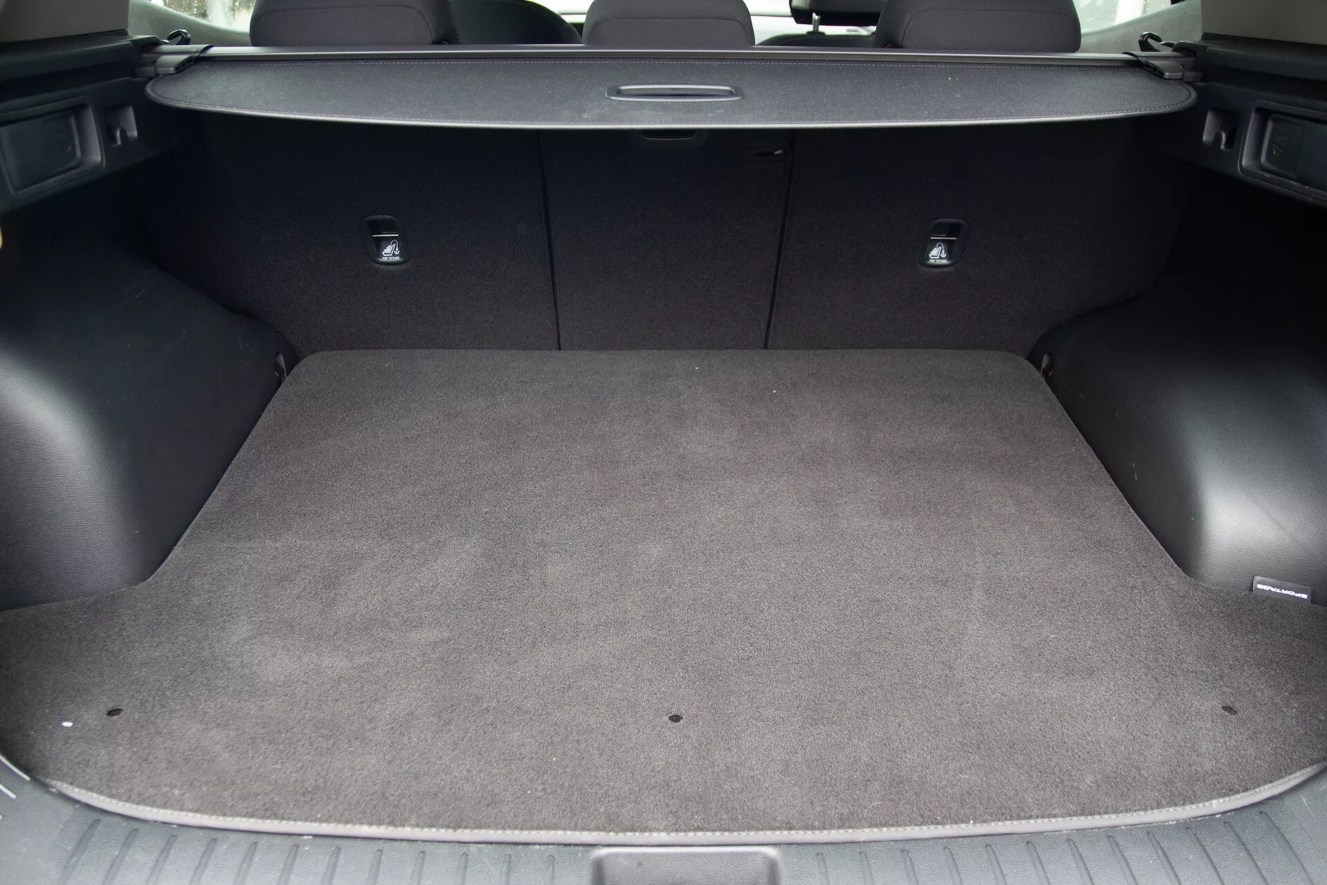 Vue de la zone de chargement du Kia Sportage 2022 montrant l'intérieur moquetté, la surface de chargement plate, les crochets d'arrimage intégrés, les points d'ancrage pour sièges d'enfants avec système LATCH et les sièges arrière rabattables 60/40 pour un espace de chargement flexible
