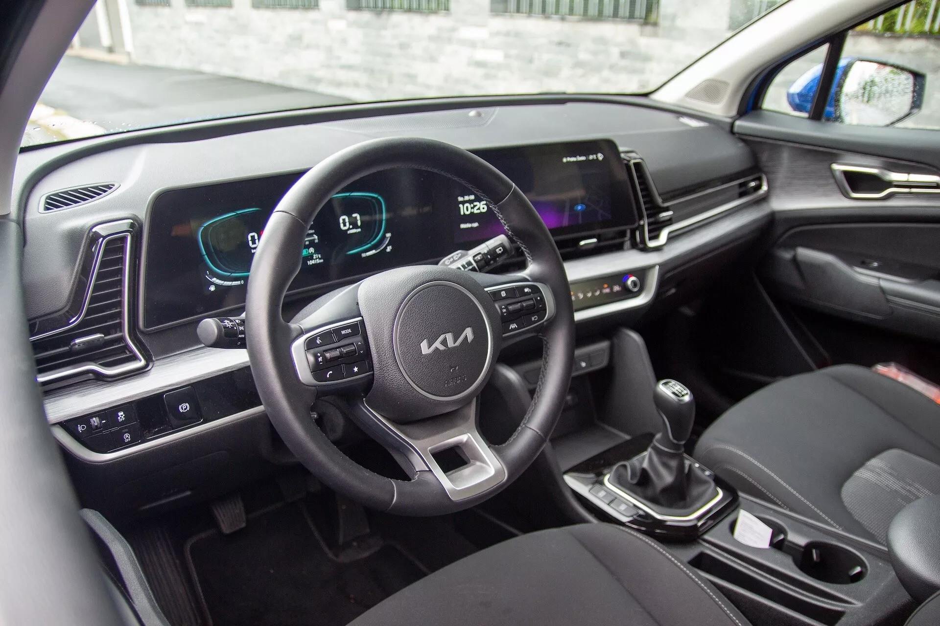 Intérieur de la Kia Sportage 2022 montrant le volant avec boutons de commande, tableau de bord numérique et écran d'infodivertissement