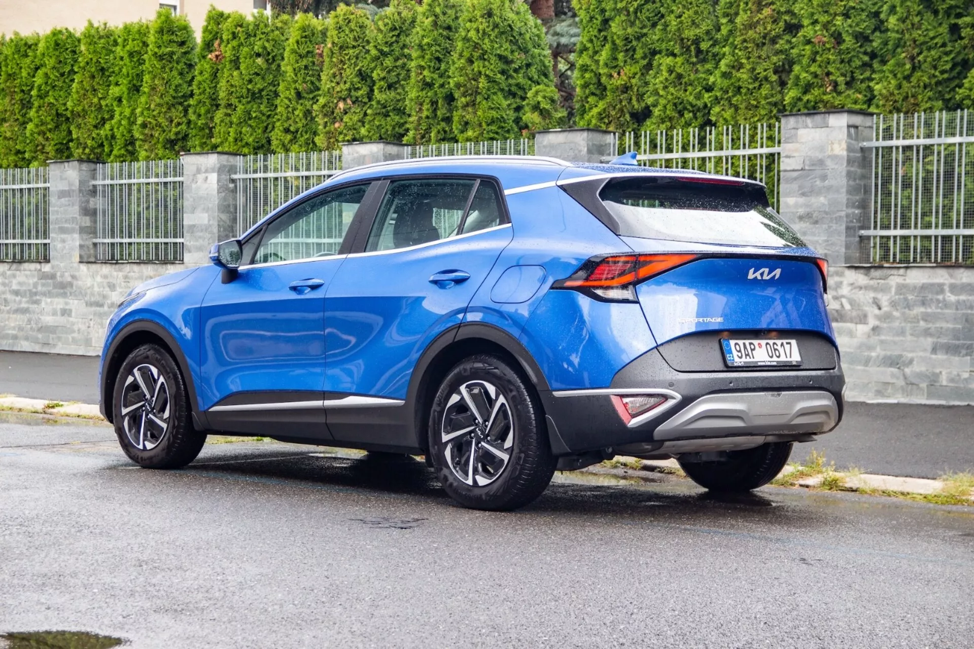 SUV compact Kia Sportage 2022 en bleu, présentant des feux arrière LED, des capteurs de stationnement intégrés, un profil latéral dynamique avec ligne de ceinture ascendante, des roues en alliage à multiples branches, des rétroviseurs latéraux avec clignotants, une antenne aileron de requin et des barres de toit, capturé depuis un angle arrière de trois quarts mettant en évidence la conception et les caractéristiques