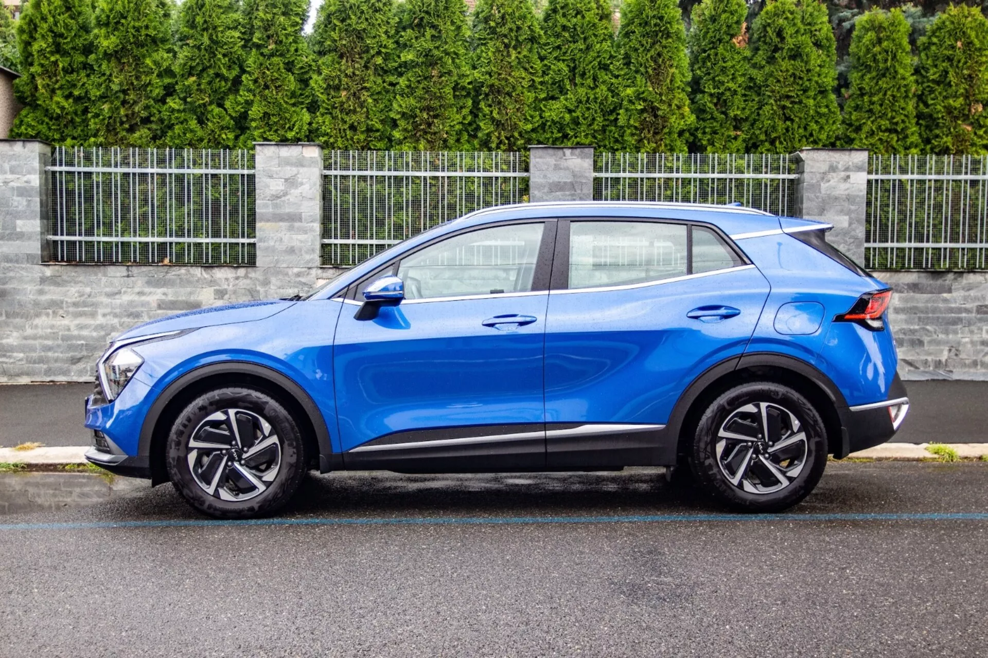 SUV crossover Kia Sportage 2022 en bleu vif, présentant son design épuré et compact avec une ligne de toit inclinée façon coupé, capot profilé, unités de phares LED, jantes en alliage à cinq branches et améliorations aérodynamiques telles qu'un spoiler arrière, dans un cadre suburbain.