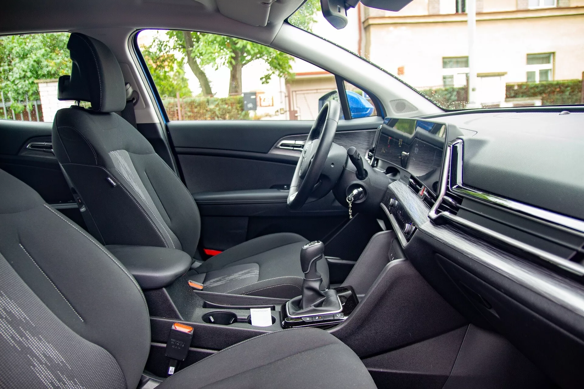 Vue intérieure du Kia Sportage 2022 du point de vue du passager arrière montrant le siège du passager avant, la console centrale avec levier de vitesse automatique, le volant à gauche et un grand écran d'infodivertissement sur le tableau de bord