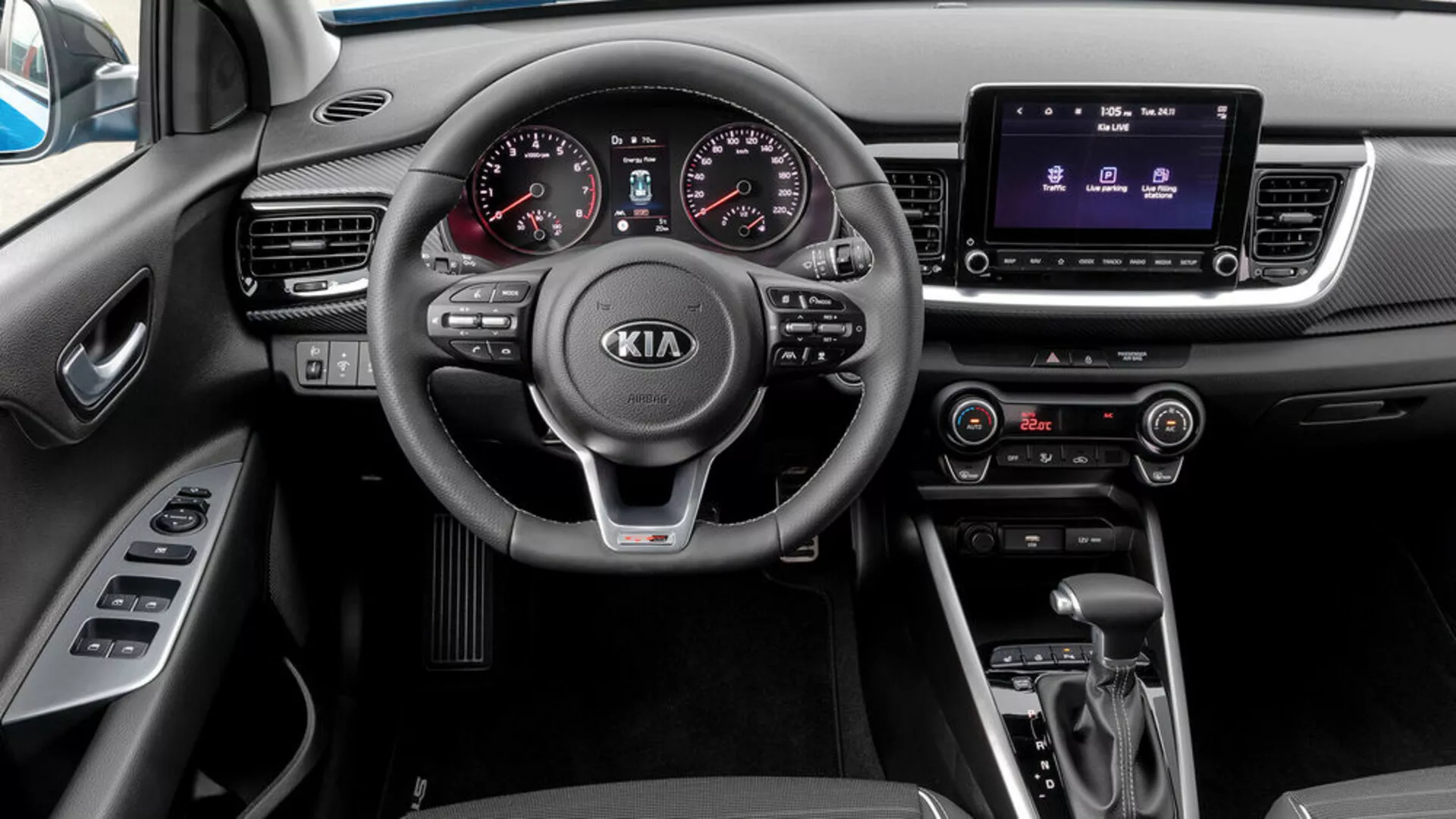 Vue intérieure d'une Kia Stonic de 2017 depuis la perspective du passager, offrant un volant à trois branches avec des commandes intégrées, un tableau de bord analogique-numérique, un système d'infodivertissement tactile, un contrôle climatique, une transmission automatique et un sélecteur de mode de conduite.