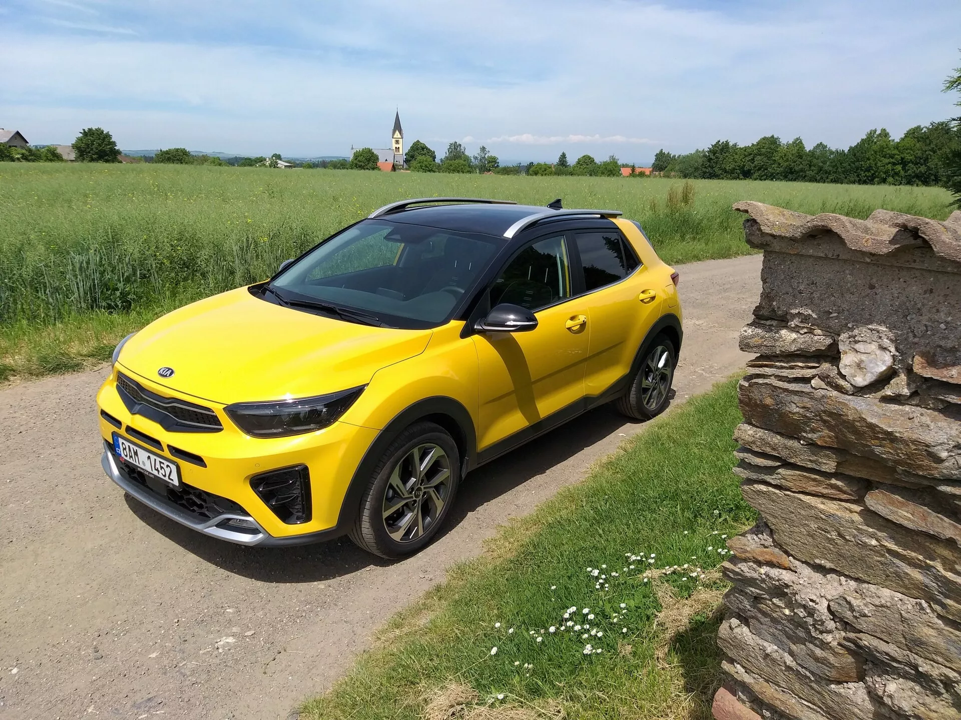 SUV compact Kia Stonic 2017 jaune vif avec toit noir, mettant en avant son design élégant et ses contours dynamiques sous un angle de trois quarts avant sur un chemin rural