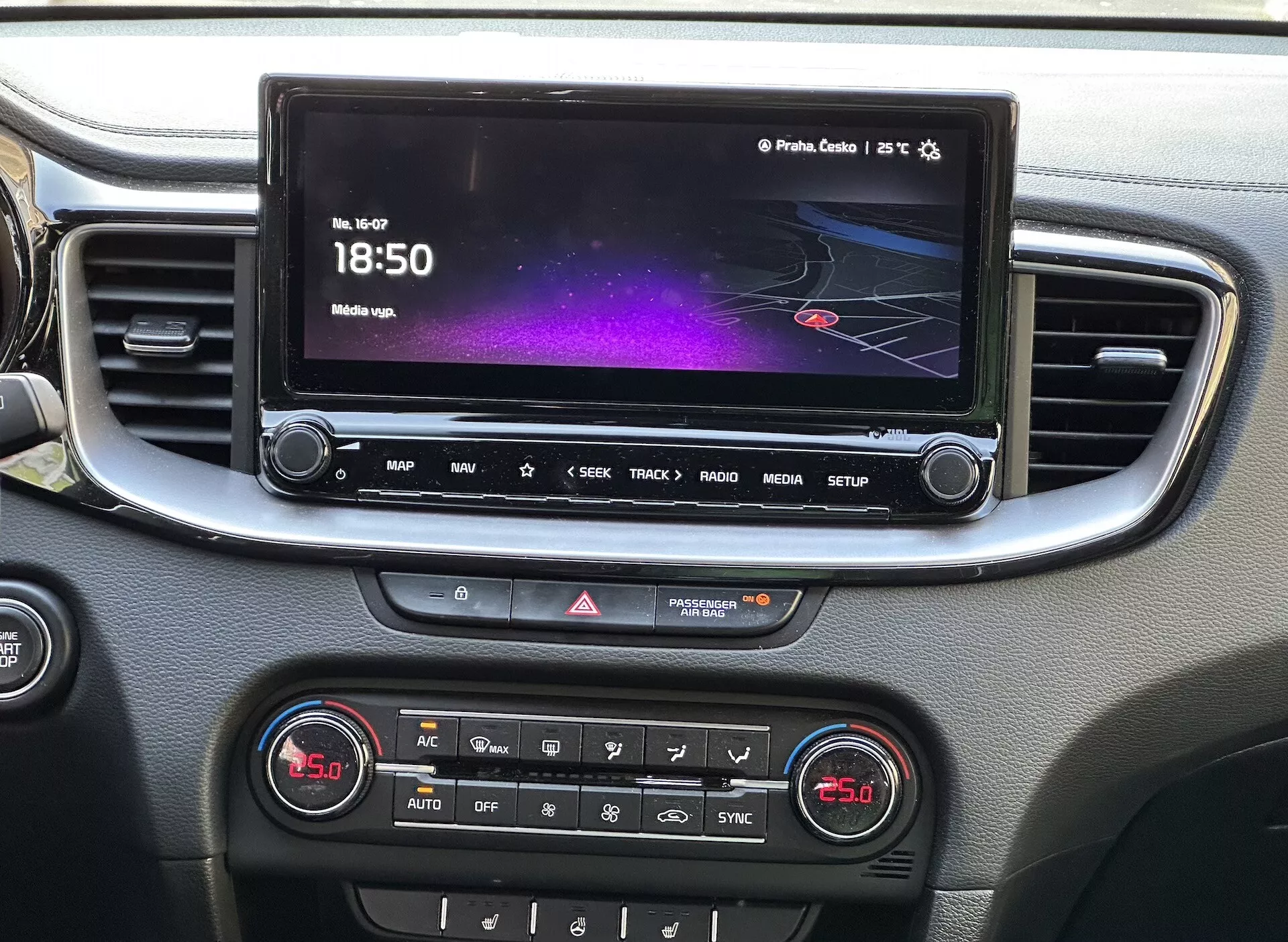 Vue détaillée de l'intérieur de la Kia Xceed 2022 montrant la console centrale avec un écran tactile d'infodivertissement affichant une interface colorée avec navigation et informations multimédia, une rangée de boutons d'accès rapide, contrôle des feux de détresse et un panneau de contrôle climatique à double zone, le tout encadré par un liseré argenté.