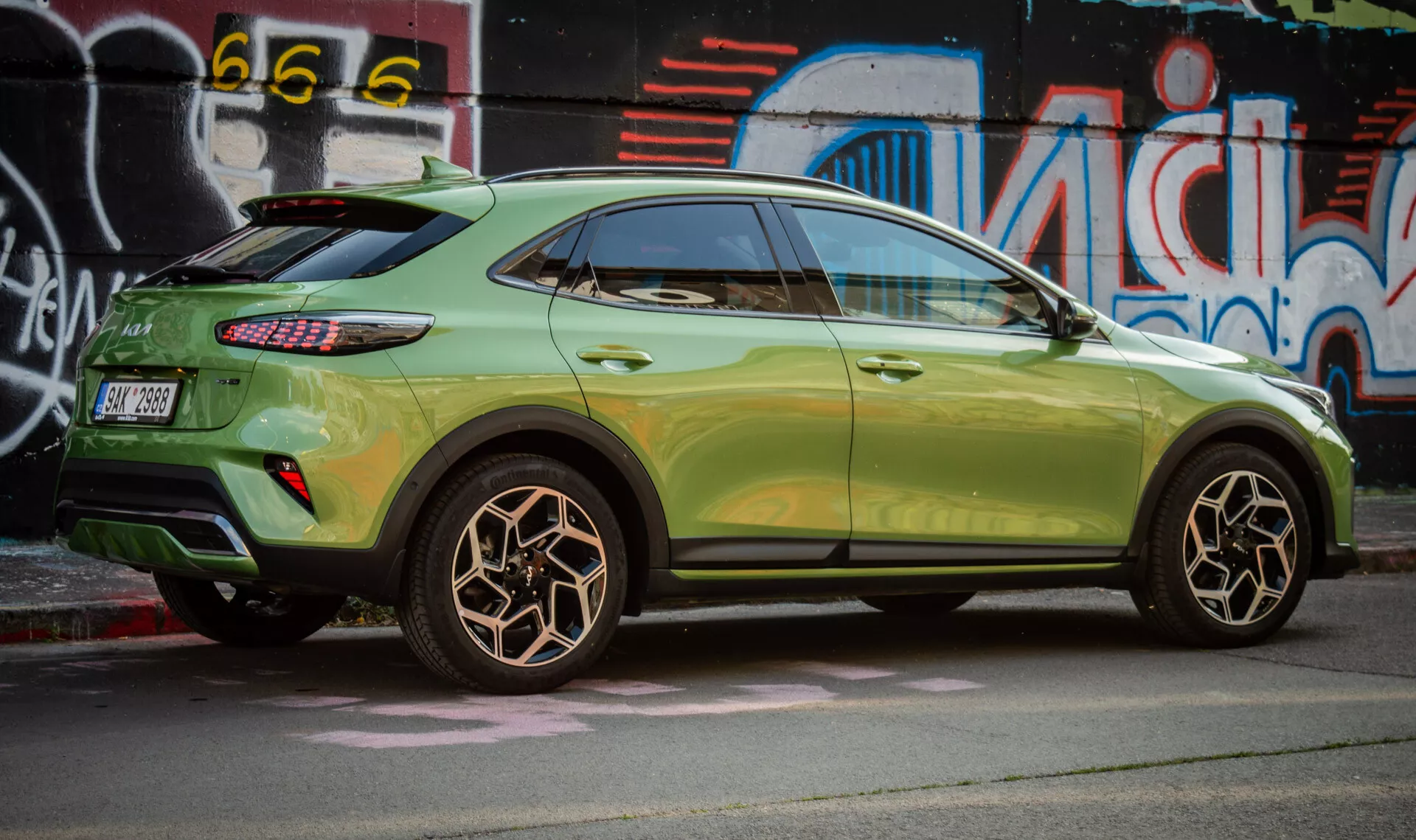 Vue de profil de la Kia XCeed 2022 mettant en avant le design de la roue arrière, la peinture verte métallisée, les feux arrière LED et le style SUV compact avec des caractéristiques aérodynamiques sur un fond d'art de rue urbain.