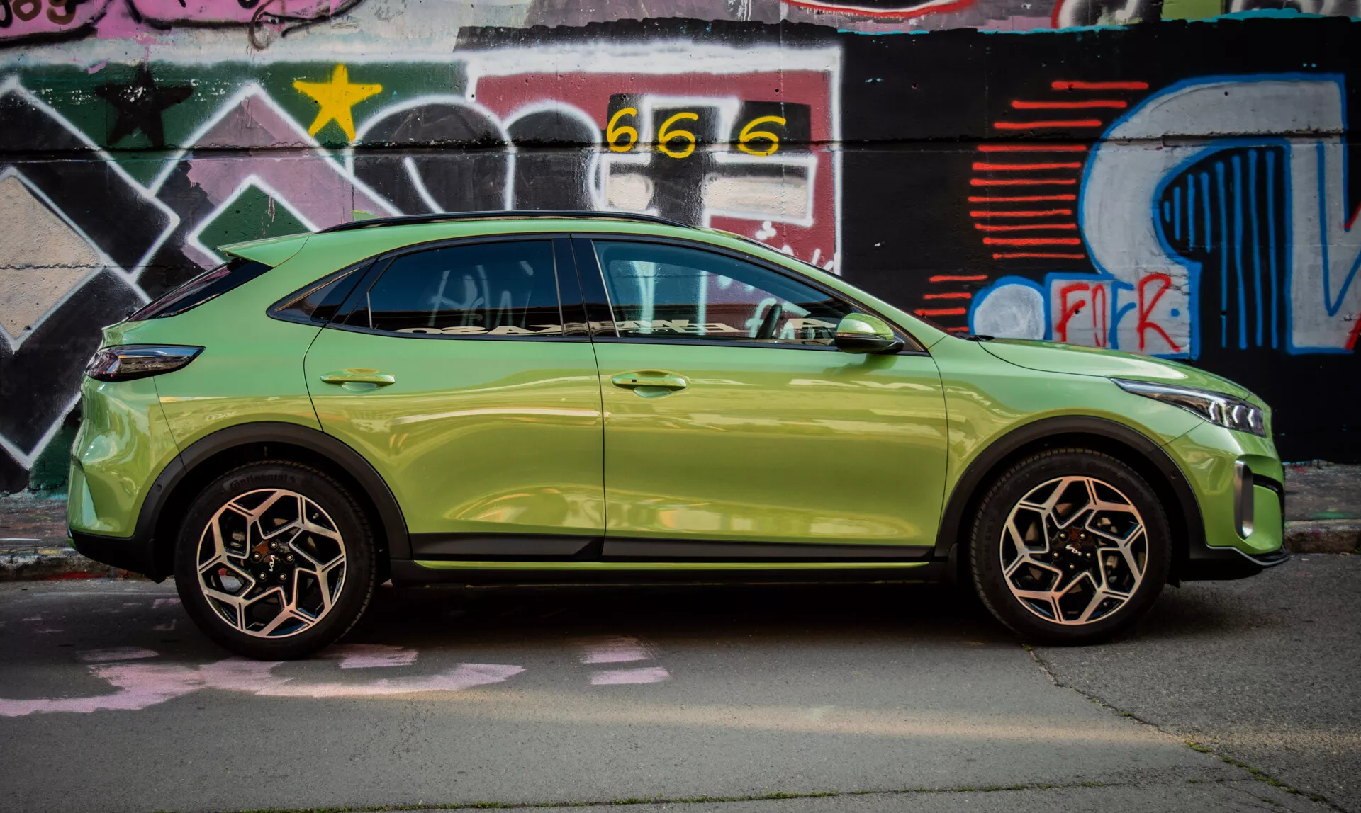 SUV compact Kia XCeed 2022 en vert lime garé devant un mur couvert de graffitis, mettant en avant son design élégant et ses fonctionnalités avancées telles que l'entrée sans clé et les clignotants intégrés dans les rétroviseurs latéraux.