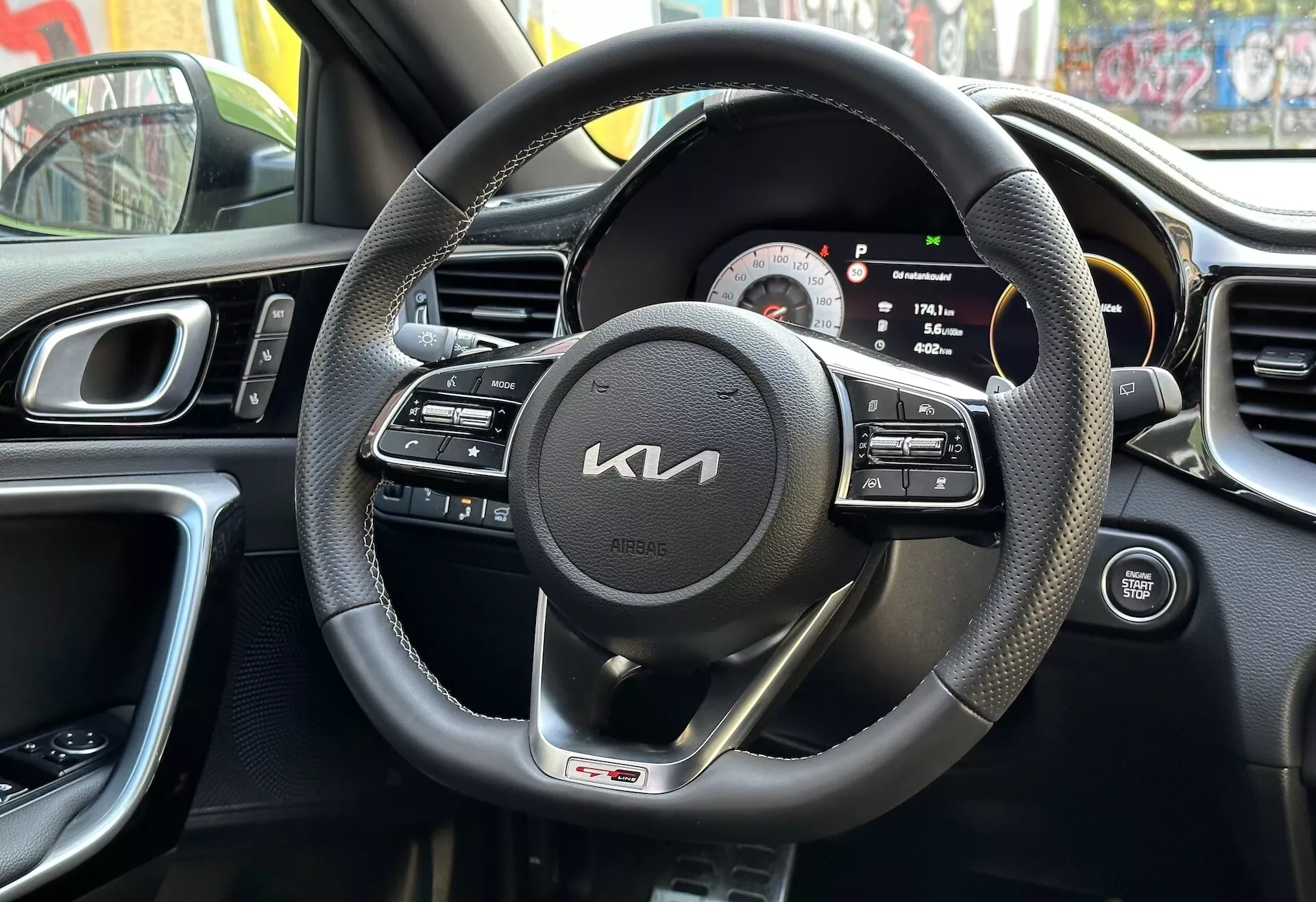 Vue intérieure du Kia XCeed 2022 depuis la perspective du conducteur avec volant en cuir noir enveloppé de commandes multifonctions et badge de ligne GT, cluster d'instruments digital-analogique, partie de la console centrale avec bouches d'air, conception ergonomique du tableau de bord, et panneau de porte du conducteur avec commandes, reflétant un environnement urbain