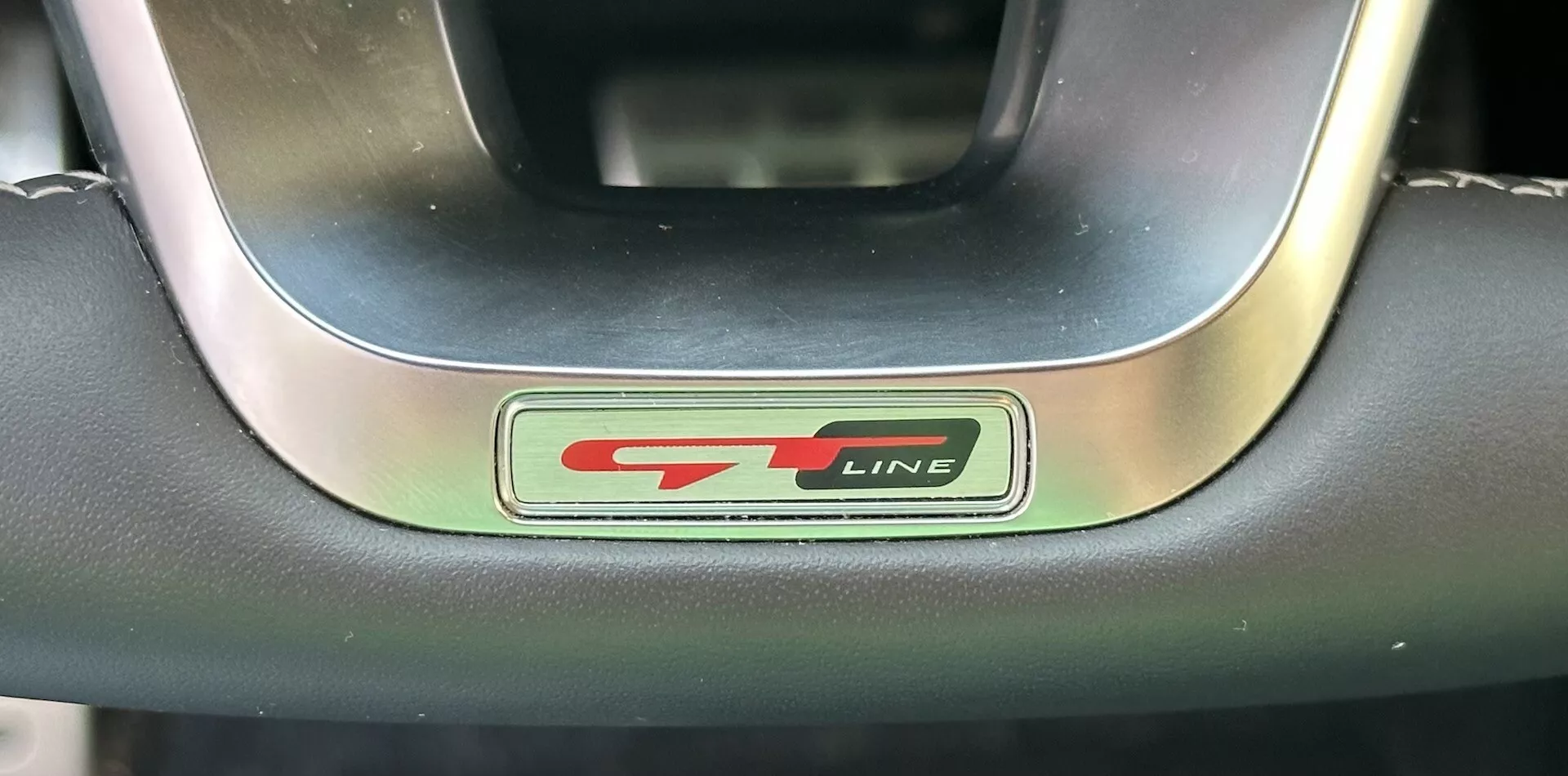Gros plan sur l'emblème du volant GT-Line Kia XCeed 2022 présentant des lettres métalliques et noires avec un accent rouge sportif, entouré d'un volant premium en cuir et métal