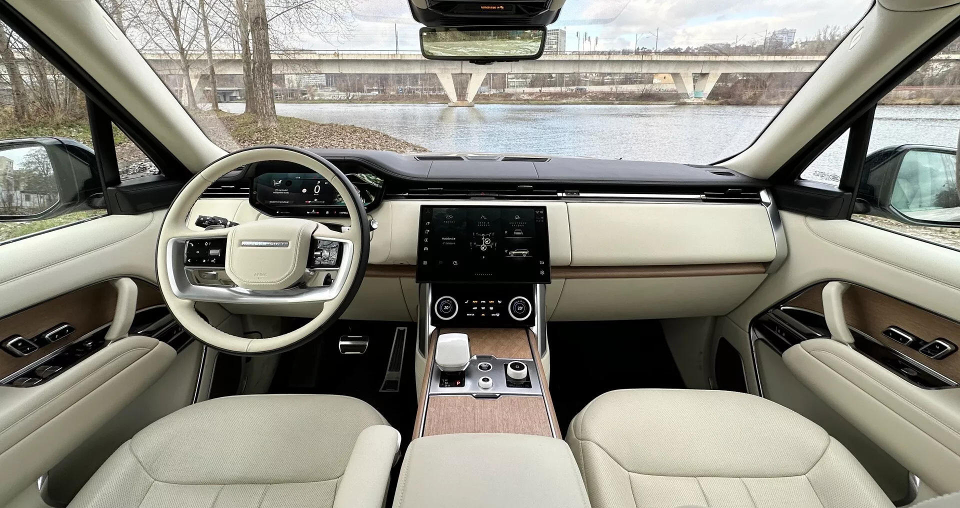 Vue intérieure du Land Rover Range Rover 2021 depuis les sièges arrières vers le tableau de bord montrant design symétrique, volant avec boutons multifonctions, système d'infodivertissement tactile, contrôle de climatisation numérique, sellerie en cuir luxueux avec accents de bois, et caractéristiques technologiques avancées
