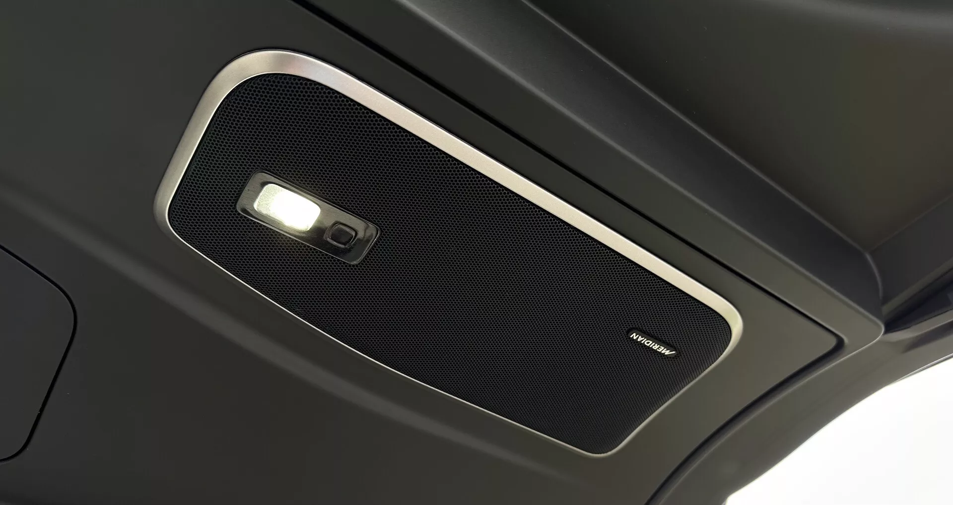 Vue rapprochée de la console supérieure intérieure du Range Rover 2021, présentant une grille de haut-parleur de haute qualité et une lumière dôme, soulignant l'acoustique premium de l'habitacle et la technologie avancée d'éclairage intérieur.