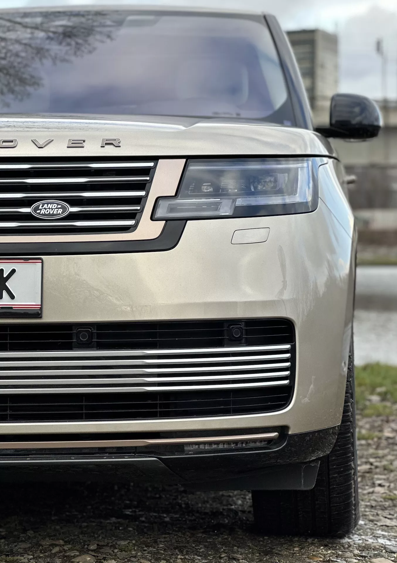 Gros plan d'un Land Rover Range Rover couleur or de 2021 mettant en évidence le quart avant gauche, soulignant la hauteur et la stance du véhicule avec un focus sur le capot, la calandre, le phare LED, le pare-chocs et le pneu toutes saisons, indicatif du luxe et de la capacité tout-terrain.