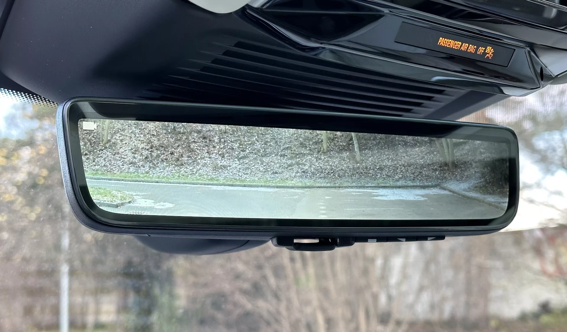 Vue rapprochée du rétroviseur intérieur électrochromique auto-assombrissant d'un Range Rover 2021, mettant en lumière son design sans cadre, les caractéristiques de la cabine intérieure, et la scène reflétée des environs extérieurs stationnaires