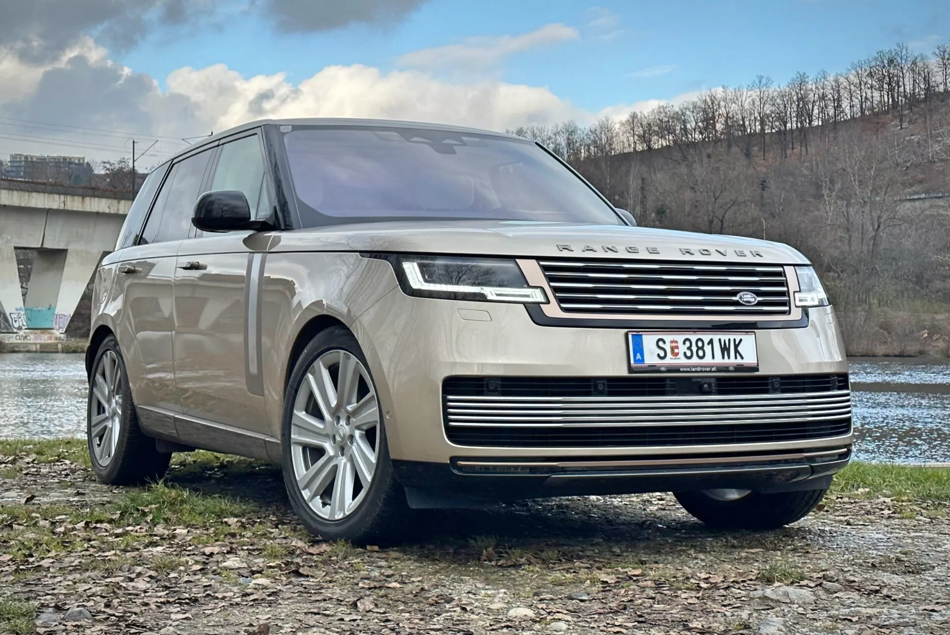SUV de luxe Land Rover Range Rover 2021, vue avant trois quarts mettant en avant la calandre chromée, phares LED, jantes en alliage à multiples branches et design aérodynamique, stationné en extérieur près d'une rivière et d'un pont