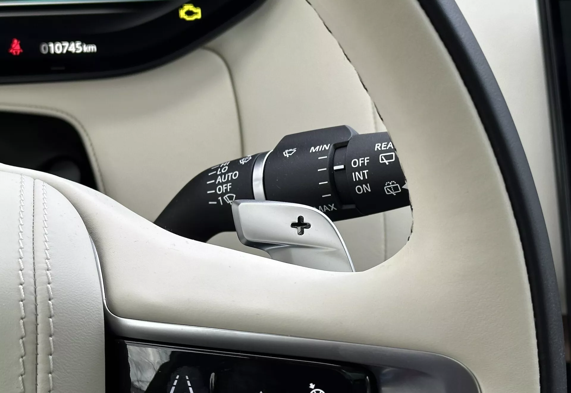Vue rapprochée de l'intérieur du Land-Rover Range-Rover 2021 montrant la colonne du volant, la manette de commande d'essuie-glace avec plusieurs réglages incluant OFF, INT, ON, ajusteurs de vitesse, et AUTO pour les essuie-glaces automatiques à détection de pluie, plus une option d'essuie-glace arrière. La partie visible du tableau de bord affiche 10745 km, le tout contre un intérieur premium noir et crème.
